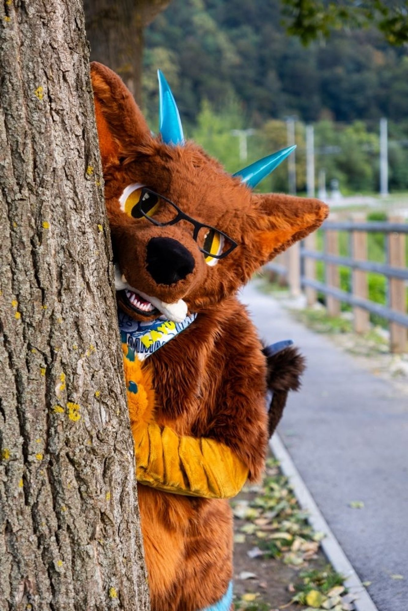 A photo of me in fursuit, peeking out behind a tree trunk. The left hand is laying at the trunk. Expression is rather curious.