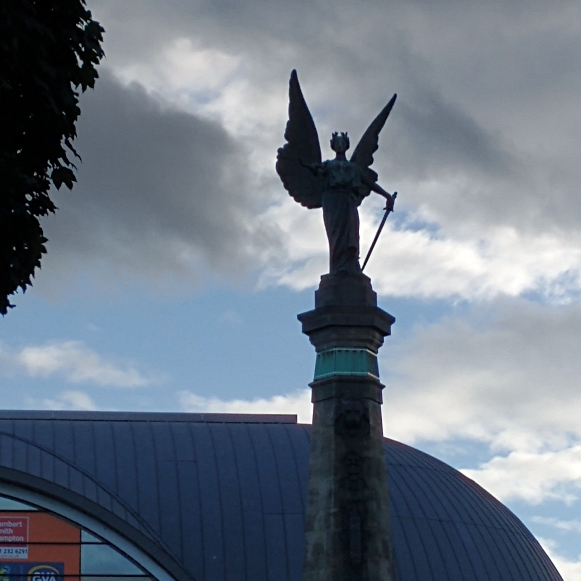 Statue of a winged female figure with a sword, against a moody sky