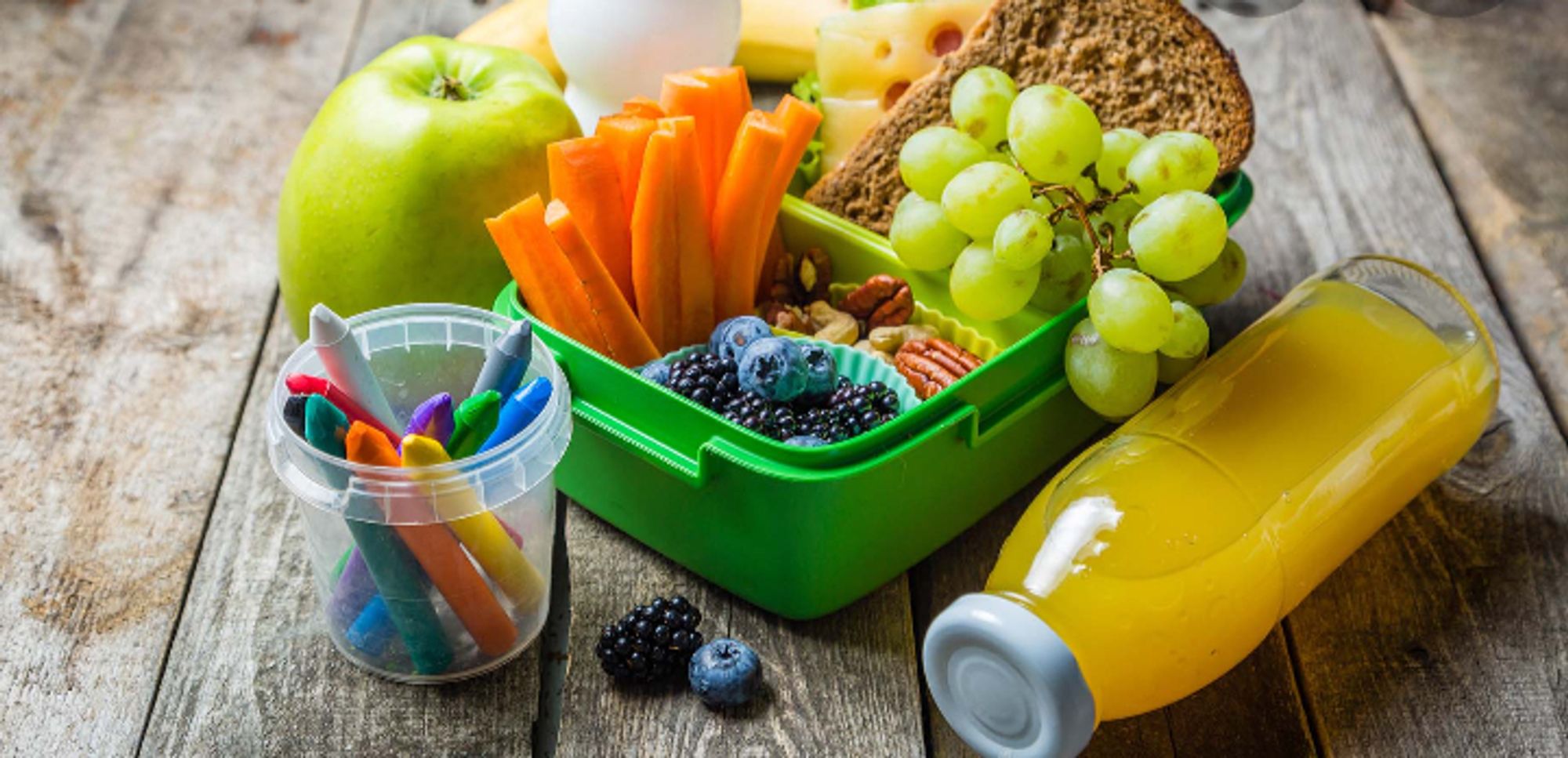 Lunchbox with sandwiches, fruit and nuts, fruit juice and a cup of crayons for colouring.