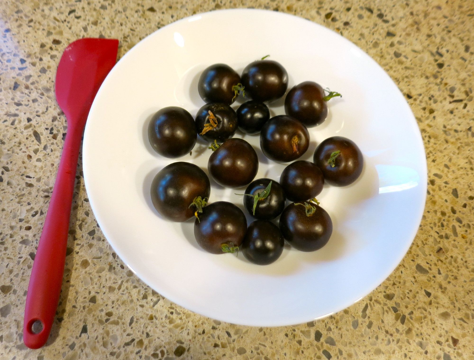 Purple-black tomatoes in a white dish, cherry-tomato sized.