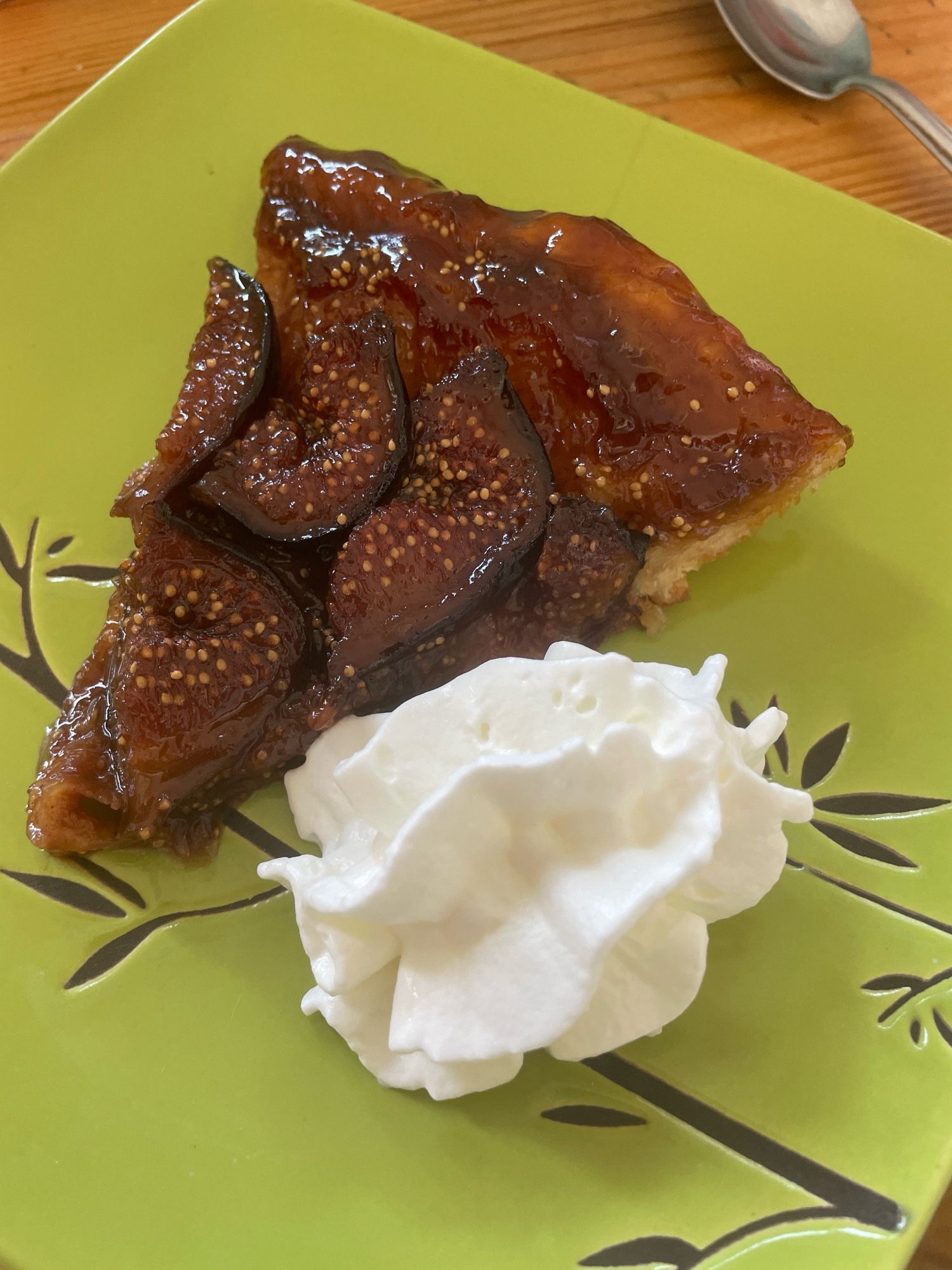 Une part de tarte tatin  aux figues avec de la chantilly sur une assiette verte .