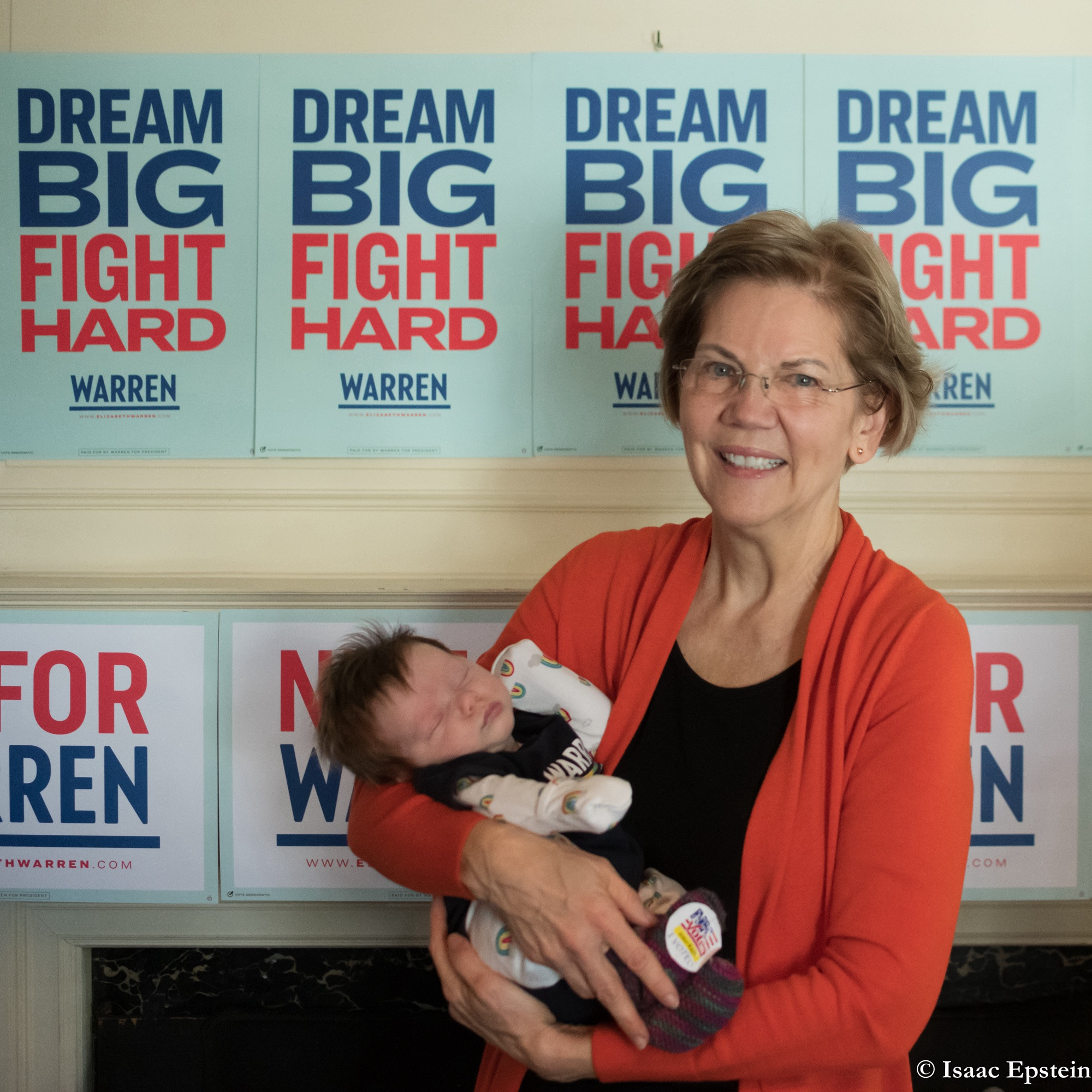 Elizabeth Warren holding my sleeping 7-week old son in late 2019. the signs behind them say “Dream Big, Fight Hard”