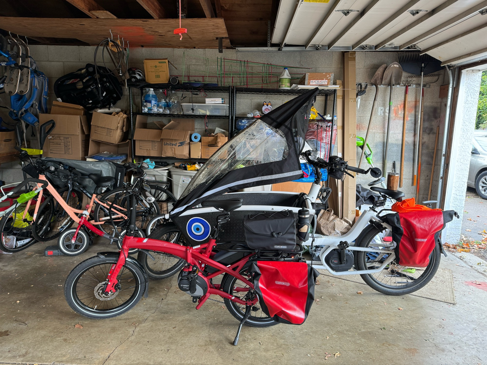 A garage with 5 visibile bikes, including a Tern Vektron foldie and a Urban Arrow bakfiets. On the far right you can see a sedan parked outside the garage