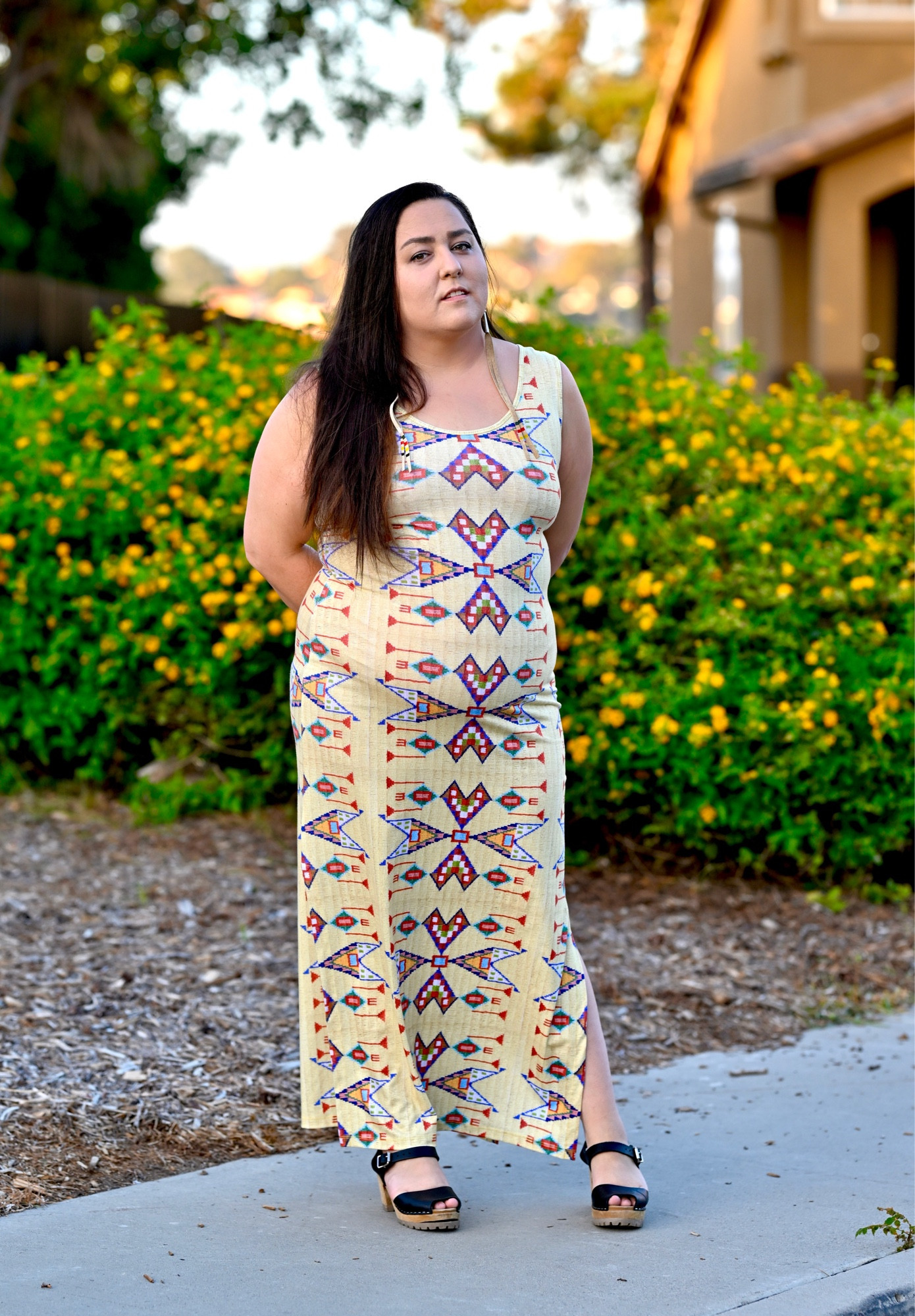 picture of me with long hair in a yellow beaded dress. In front of a sunset & yellow flowers