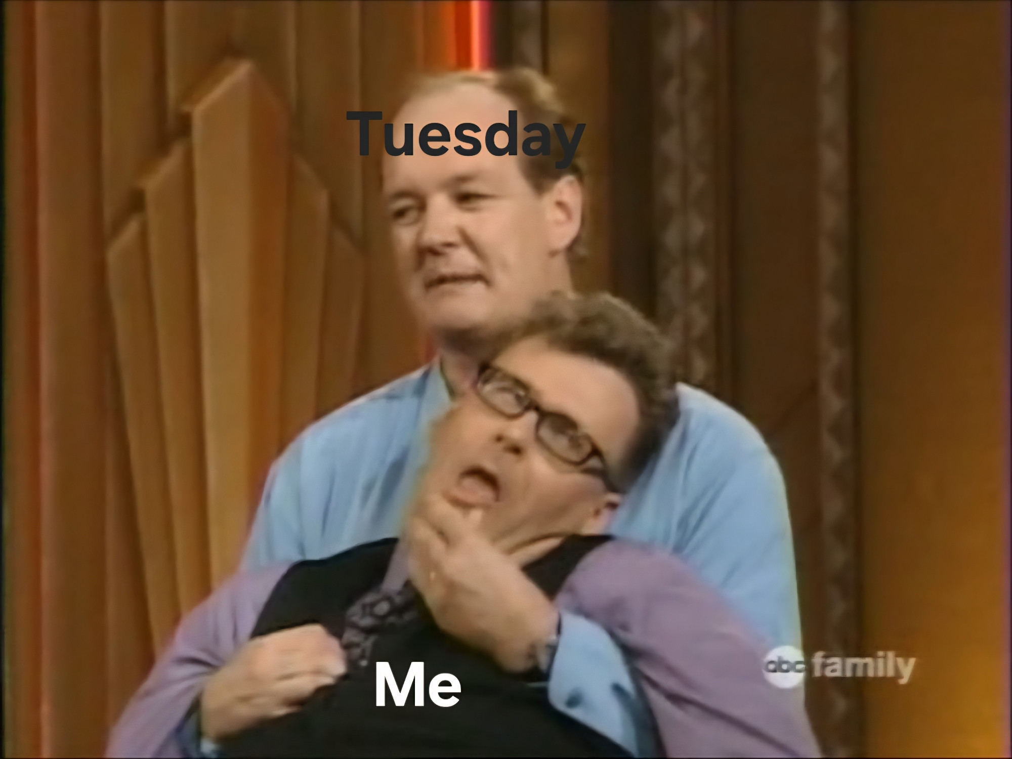 Still from a 90s episode of Who's Line Is It Anyway featuring Colin Mochrie holding a slumped Greg Proops, manipulating his mouth as part of a challenge. Colin has the word "Tuesday" written across his head in black text, whilst Greg has the word "Me" written in white text across his chest.