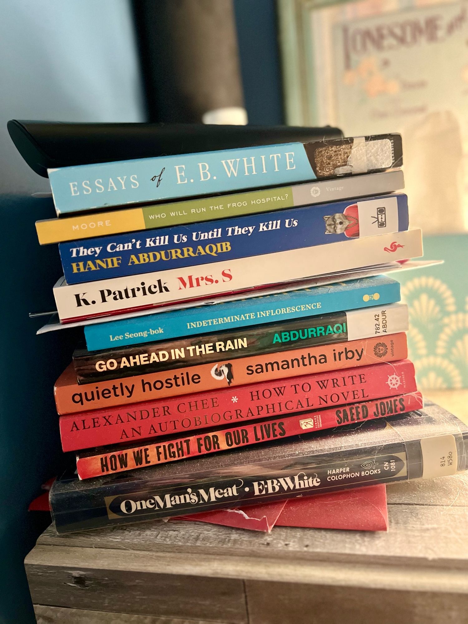 stack of books on a bedside table. mostly poetry and essay collections, several with old library stickers because they were used books when purchased.