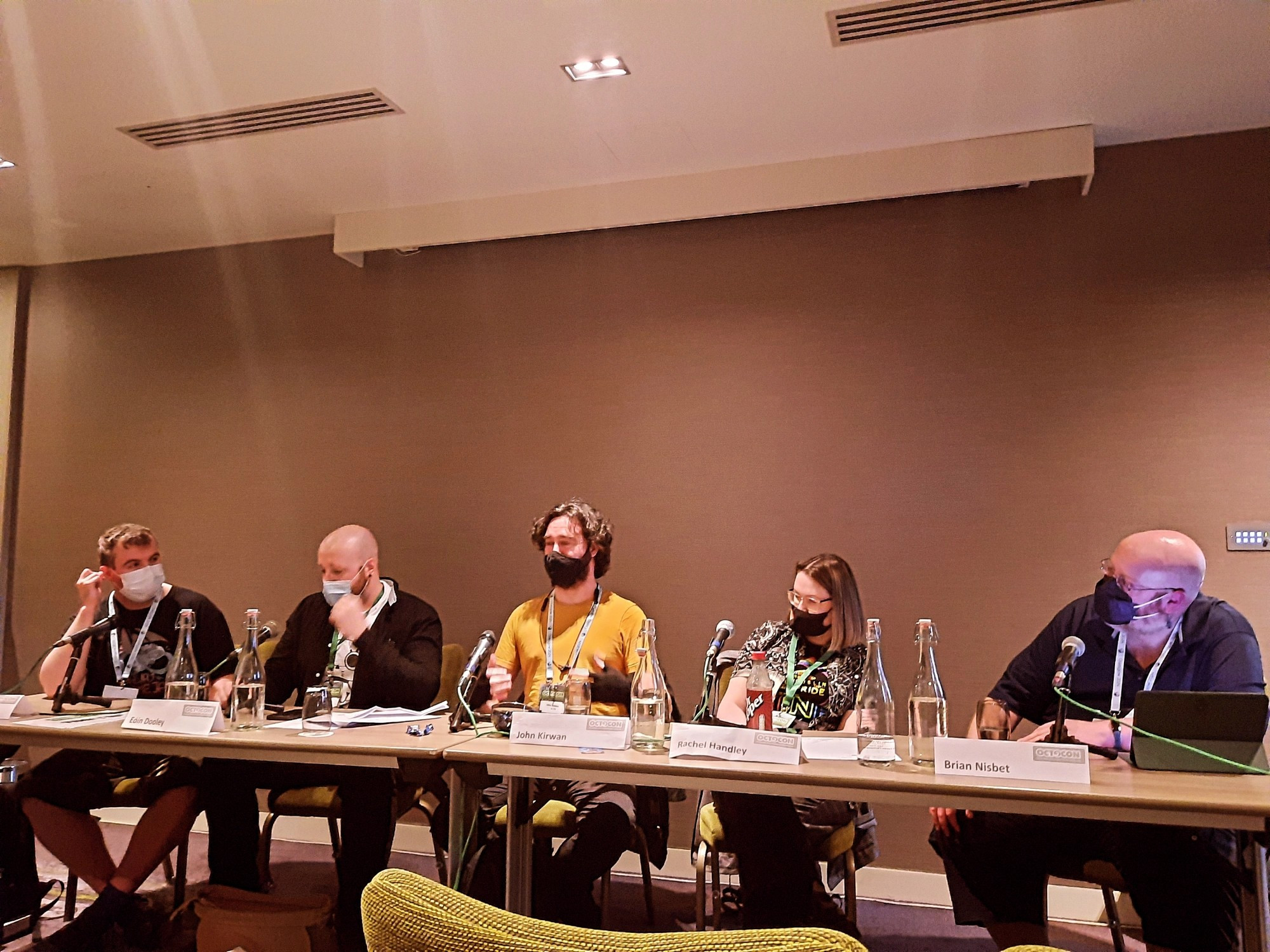 Sitting at a long table with microphones are Craig Walsh, Eoin Dooley, John Kirwan, Rachel Handley, and Brian Nisbet all wearing face masks.