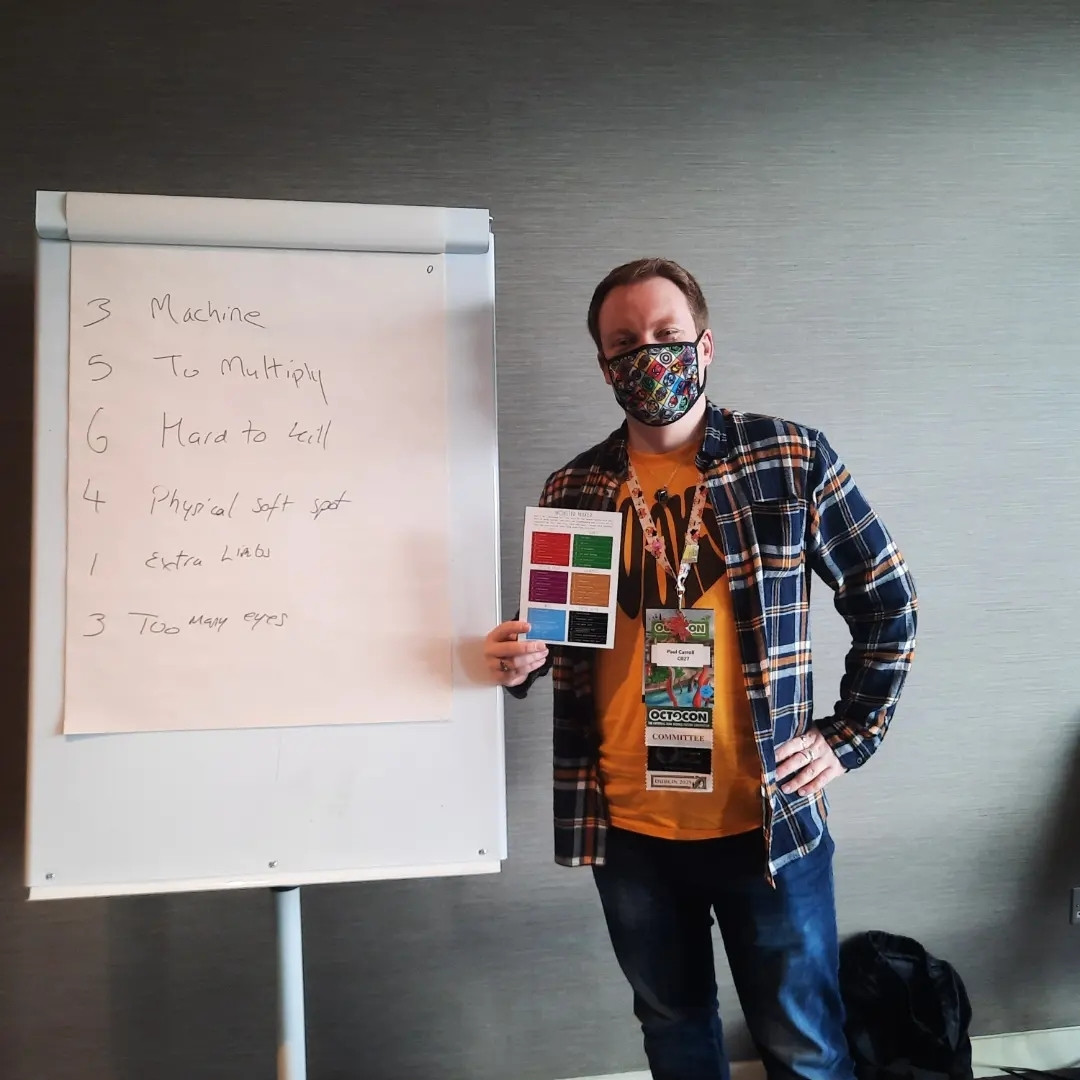 Paul Carroll standing next to a flip chart holding a coloured card used to help.make the monsters during his workshop.