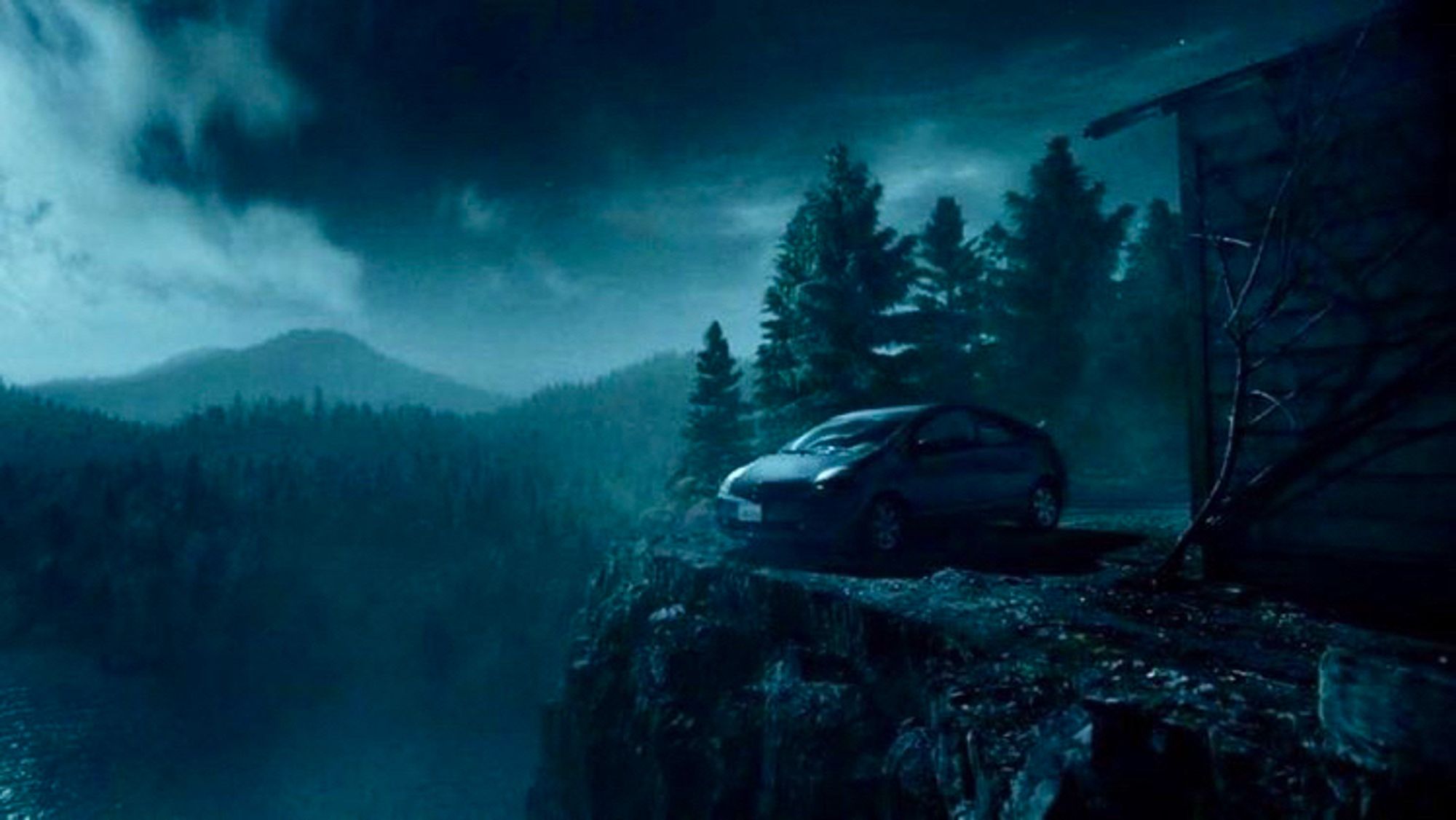 A shot from the movie Malignant where someone parks a Prius on the very edge of a jagged cliff next to a creepy house high above primeval forest and ominous clouds in the night air one of the best shots in a movie of the decade