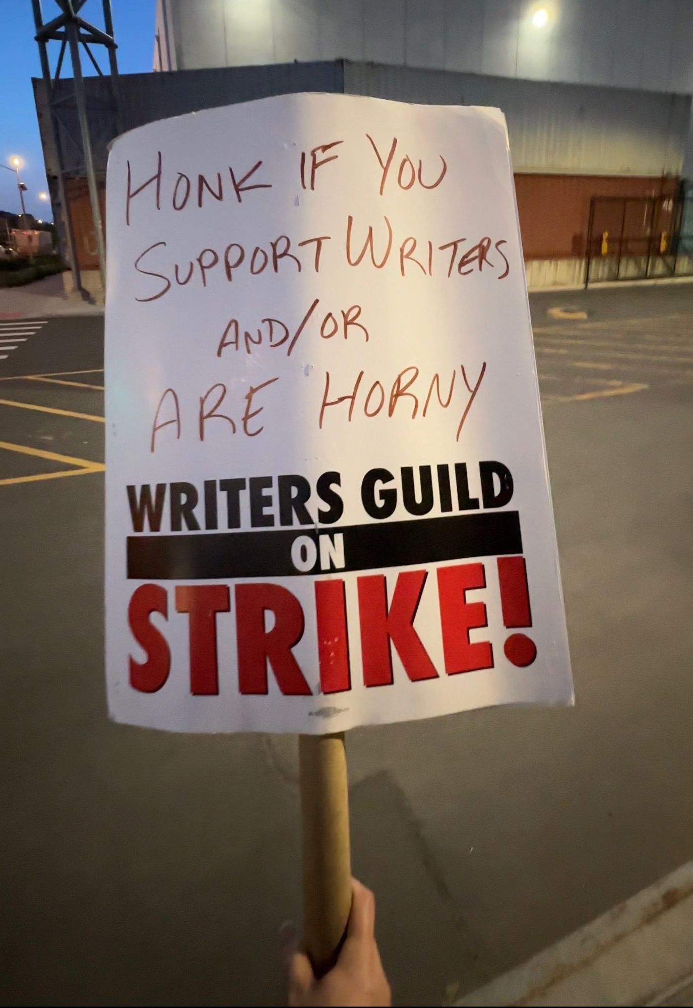 A picket sign in my hand from the WGA strike that reads ‘Honk if you support writers and/or are horny’