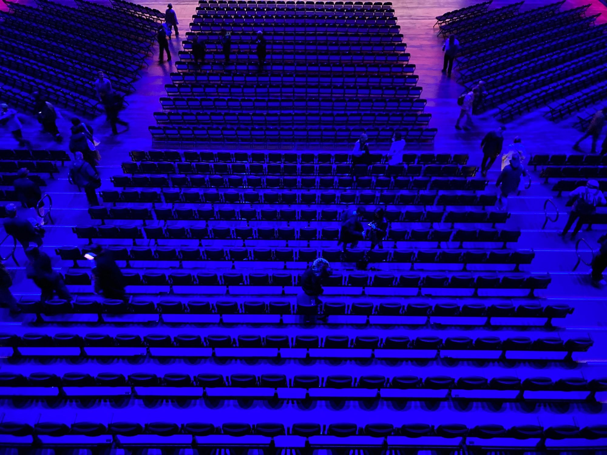 picture taken from balcony looking down at the seats below. People are leaving. The overall hue is blue transitioning to magenta at the top of the image.