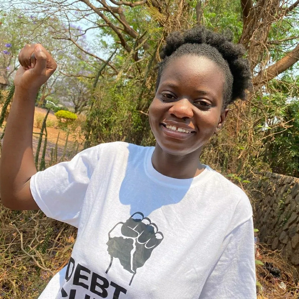 The activist woman with a raised fist. Debt for climate is written on her shirt. She smiles