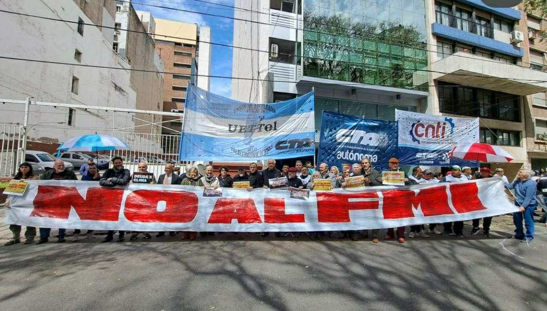 A long banner with "No Al FMI" - no to the IMF! Manny people holding debt for climate placards. Behind them are banners from argentinian unions.