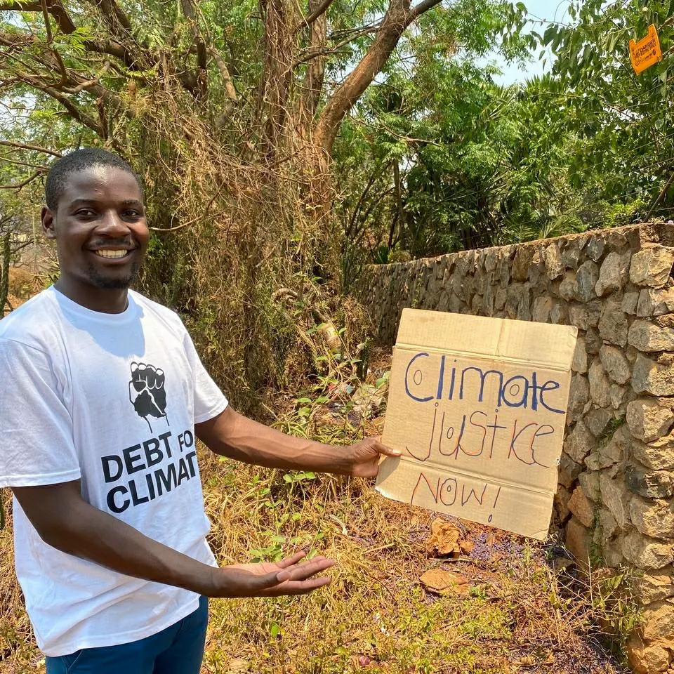 A man smiling and holding a placard that calls for climate justice now!