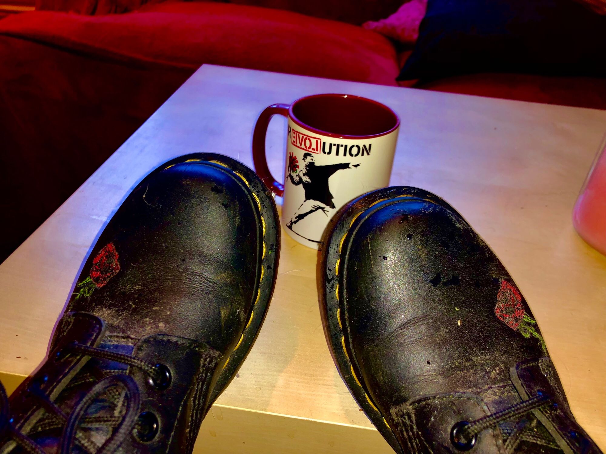 Ein paar schwarze Doc Martens mit aufgestickten Rosen. Im Hintergrund eine Tasse mit dem Aufdruck Revolution und einem Banksy Motiv.