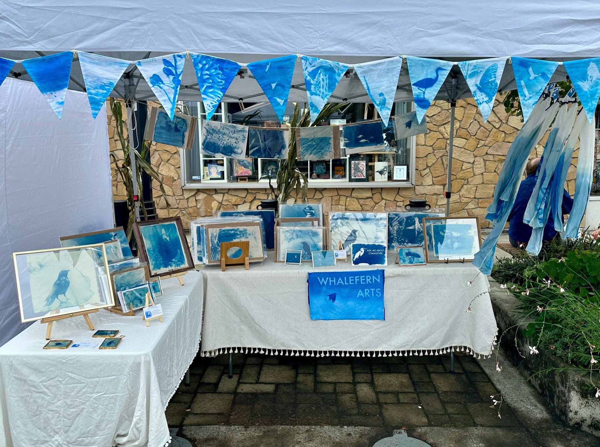 My art fair booth, featuring blue-toned prints of many animals, blue and white cyanotype silk scarves, and blue party bunting with a different animal printed on each triangular flag