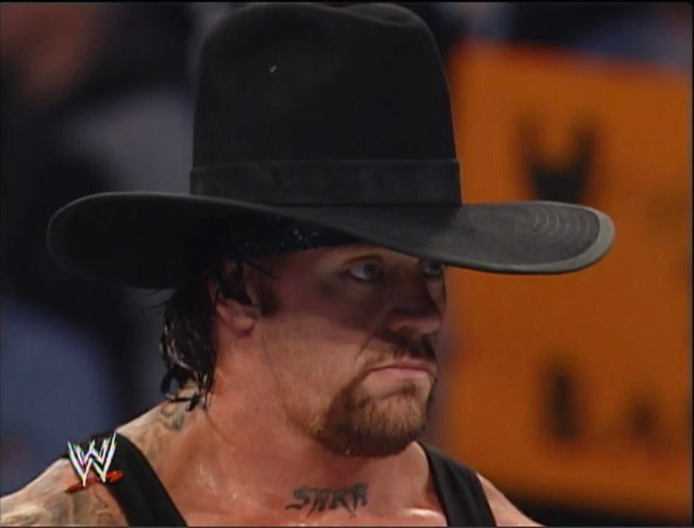 A photograph on The Undertaker, a pro wrestler, wearing a 10 gallon cowboy hat with a serious look on his face. he looks silly