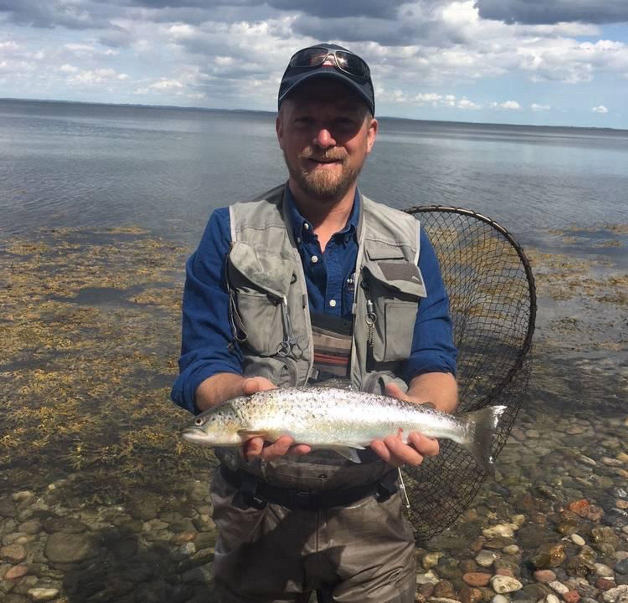 Jan Korte steht mit einem Kescher im Wasser; in seinen Händen hält er eine Meerforelle.