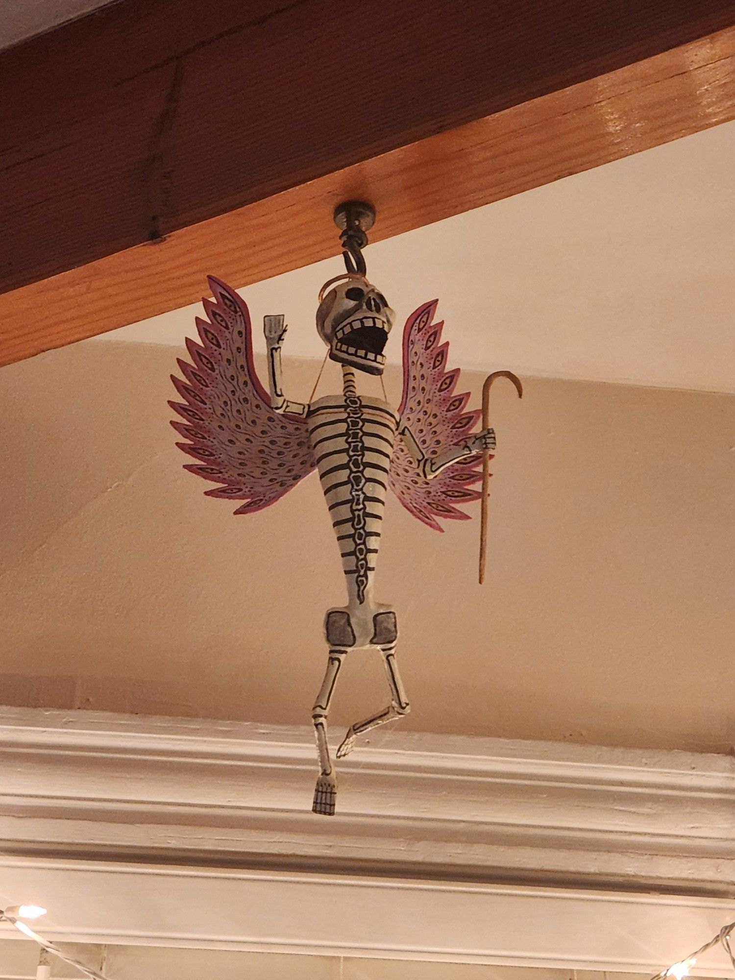 Paper mache skeleton with pink flaming wings full of eyes, a gold halo and a shepherd's crook