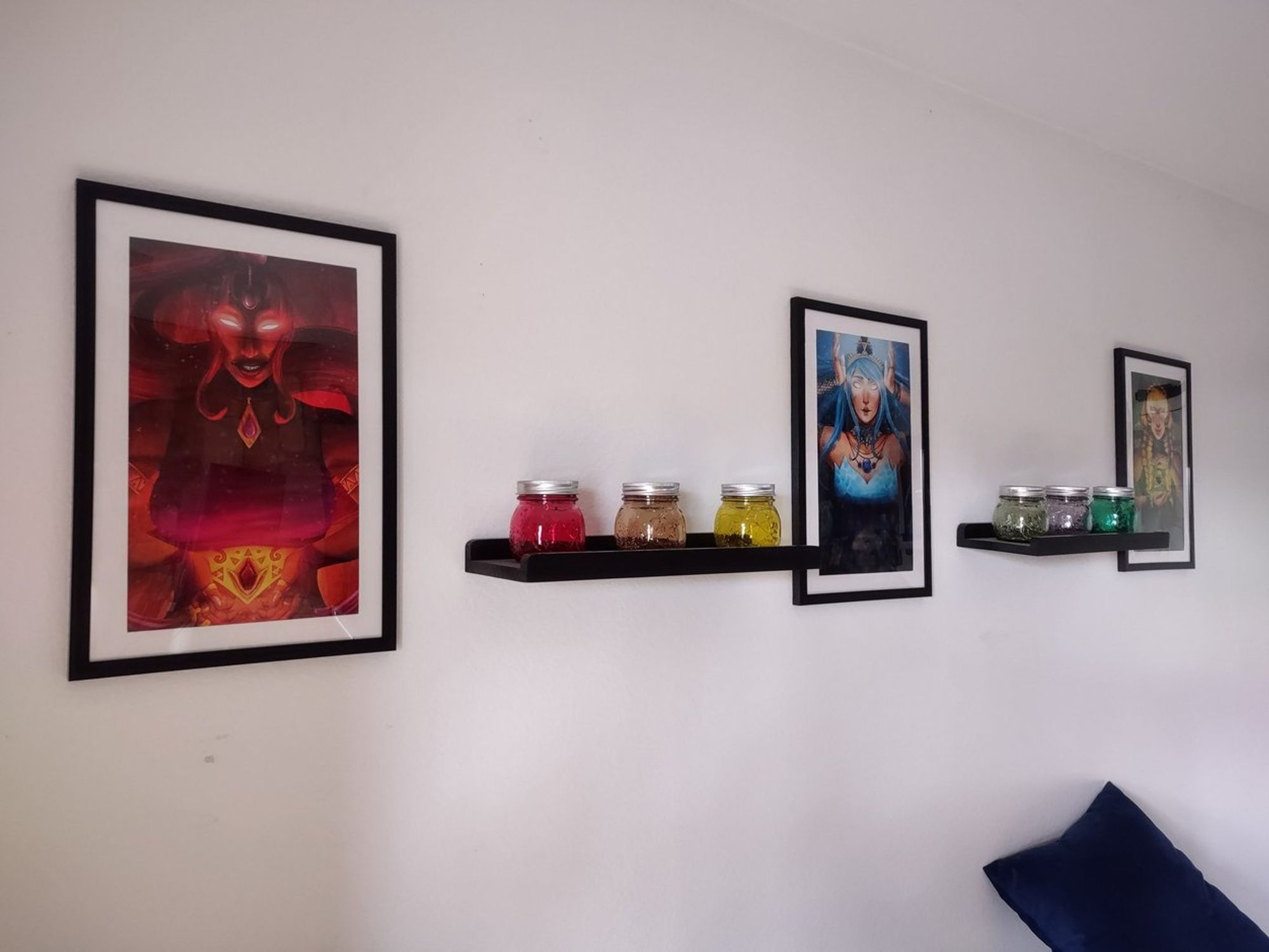 Living room wall, featuring framed artwork of Din, Nayru, and Farore, with different colored rainbow fairy jar votives representing each of the 6 sages on floating shelves between them.