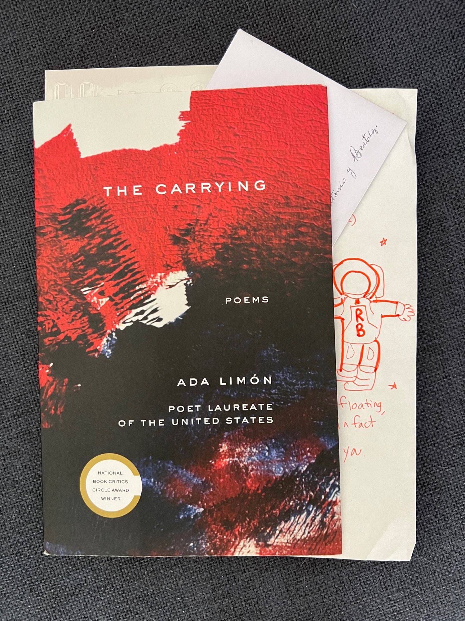 Photo showing the cover of Ada Limón’s ‘The Carrying’, a letter signed in cursive, a drawing of an astronaut with the letters RB.