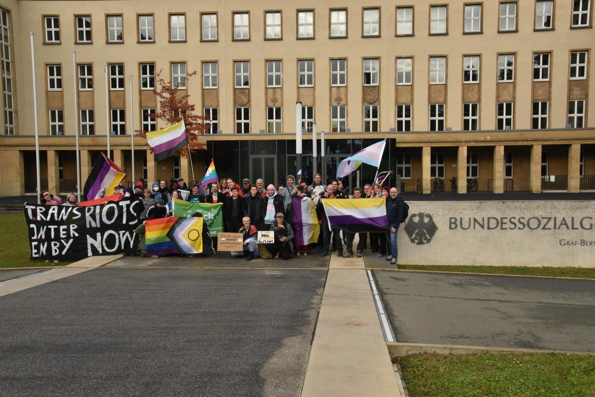 Eine Gruppe von ca 30 Menschen mit trans*, inter* und nicht-binären Flaggen steht vor dem Bundessozialgericht Kassel.