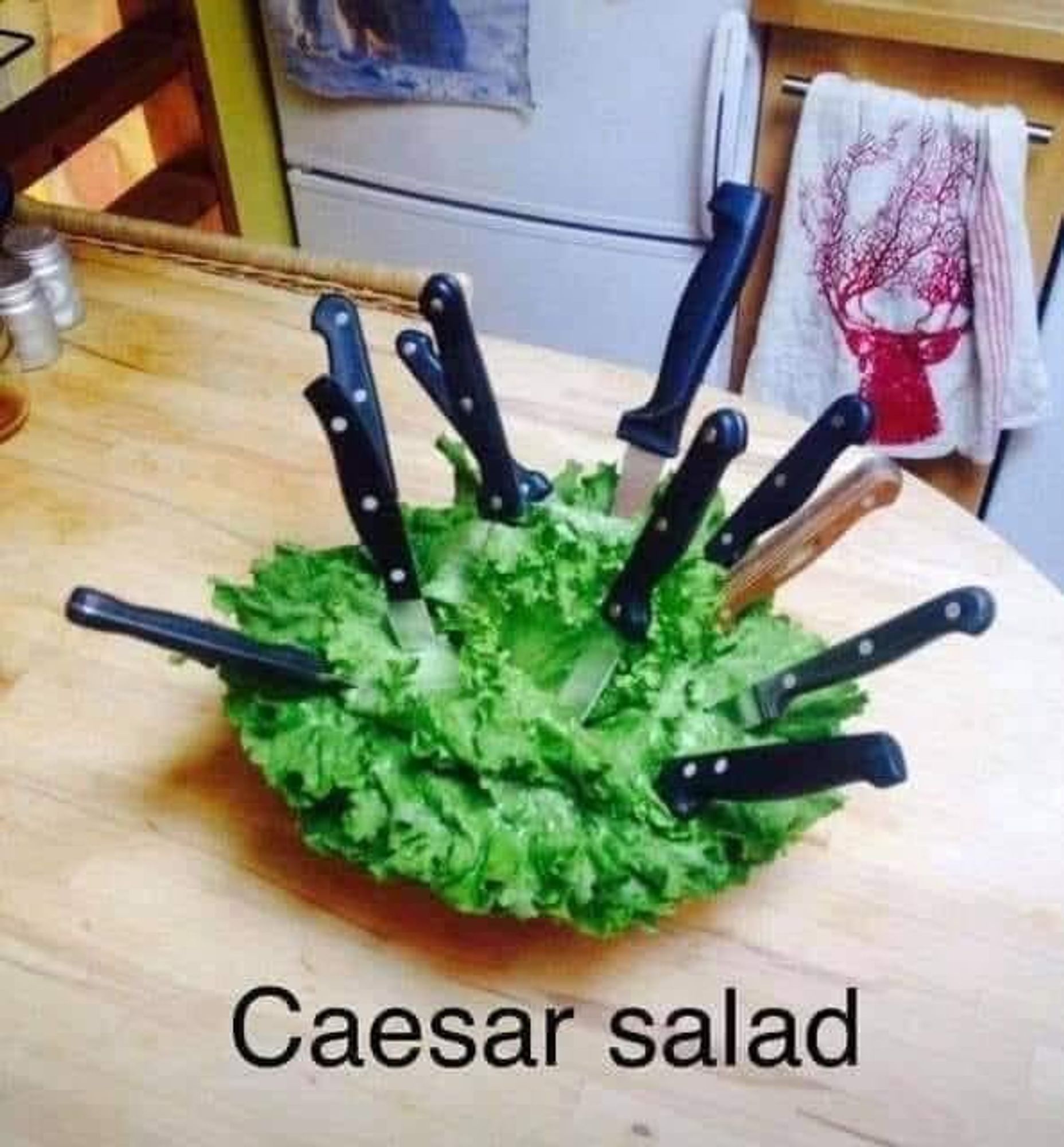 A head of Romaine lettuce with a bunch of steak knives thrust into it, with the caption that says "Caesar Salad".