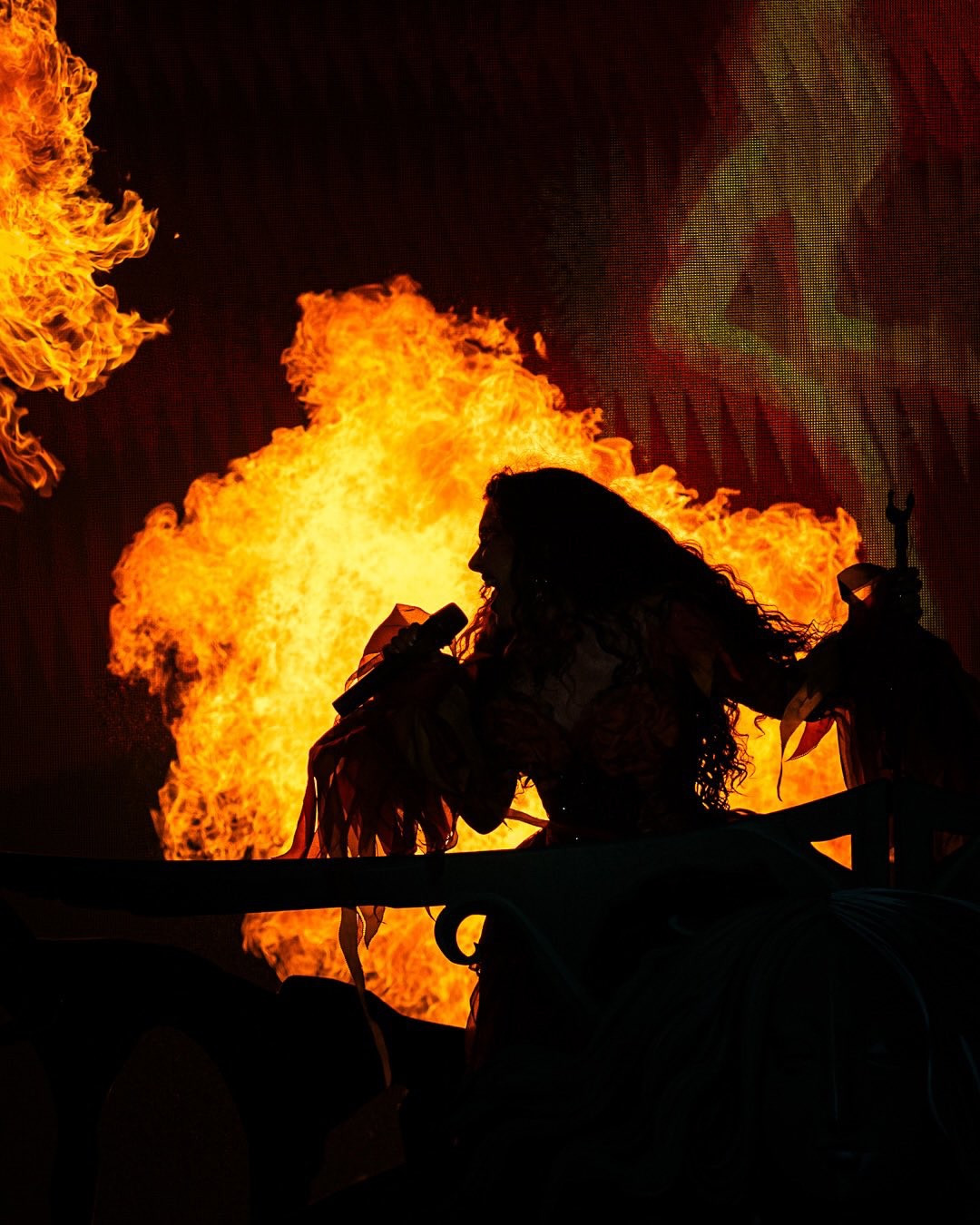 Silhouette of Chappell in a pink and orange flower costume with flame behind her 
