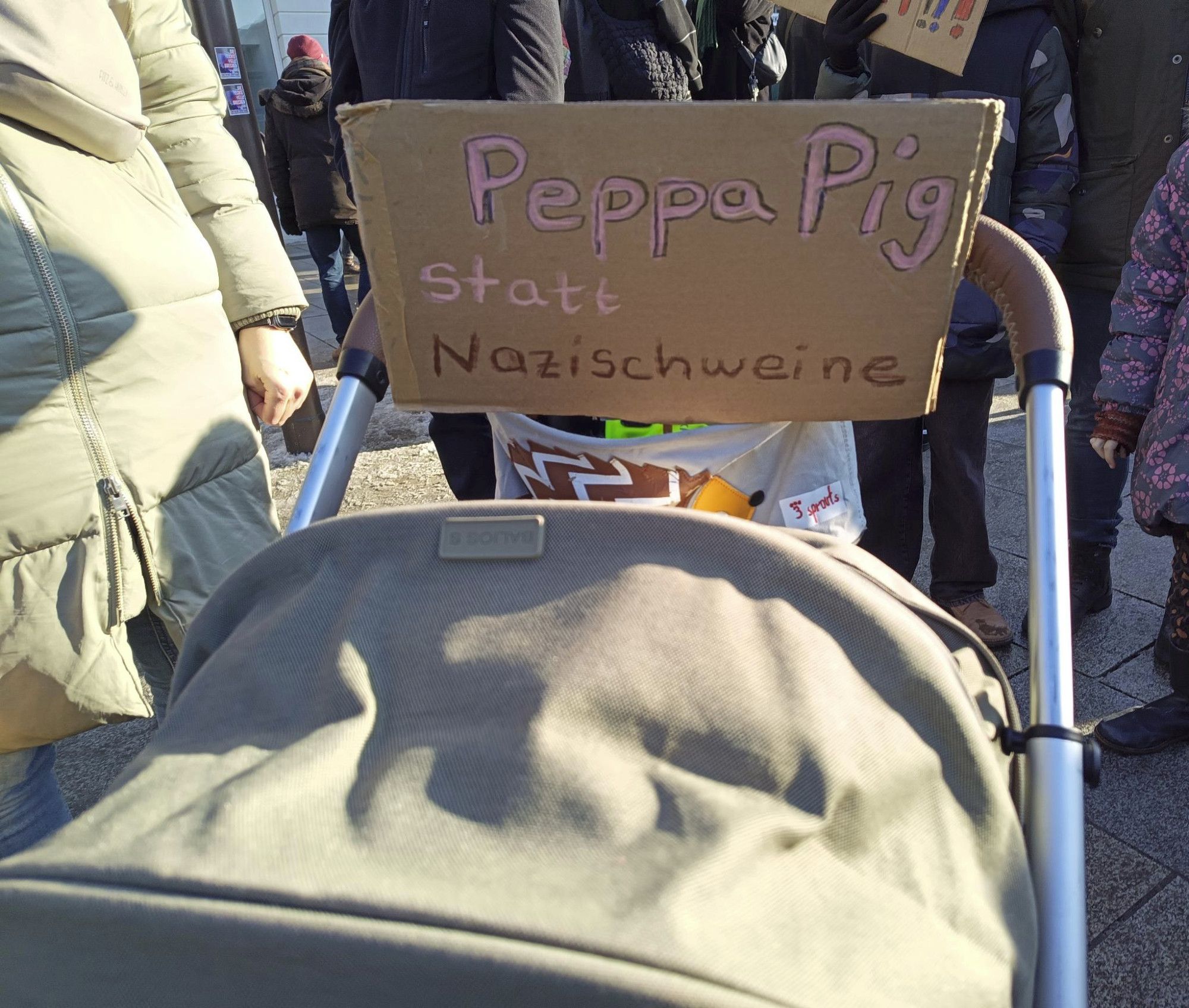 Kinderwagen mit Pappschild "Peppa Pig statt Nazischweine", letzteres in Kackbraun geschrieben, der Rest in Pink