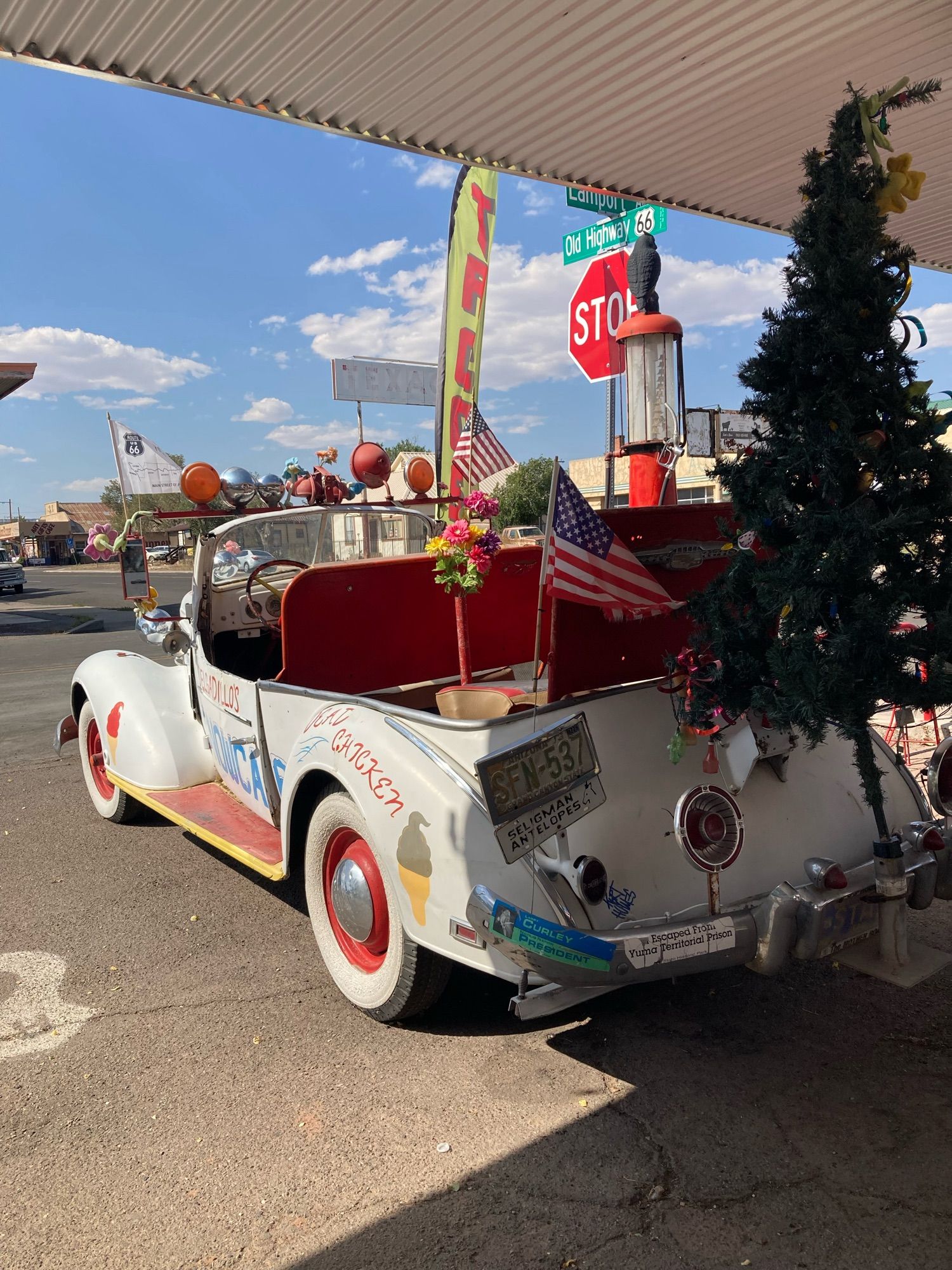 A vintage white convertible decorated with an American flag and a Christmas tree poking out of the back. A banner waves “TACOS”.