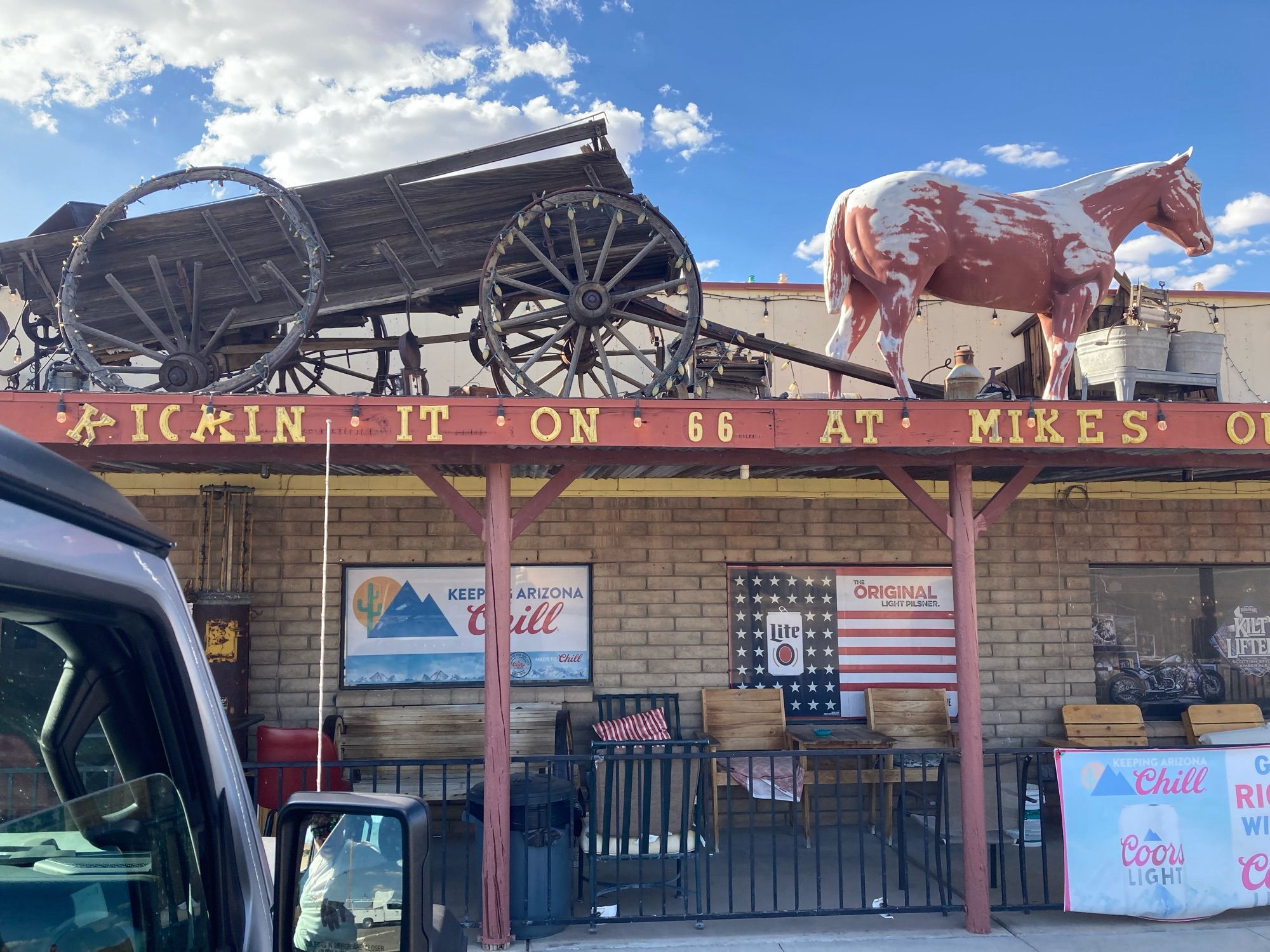 The front of an old bar with an old wagon and horse sculpture on the patio roof. Lettering reads “Kicking it on 67 at Mike’s”.