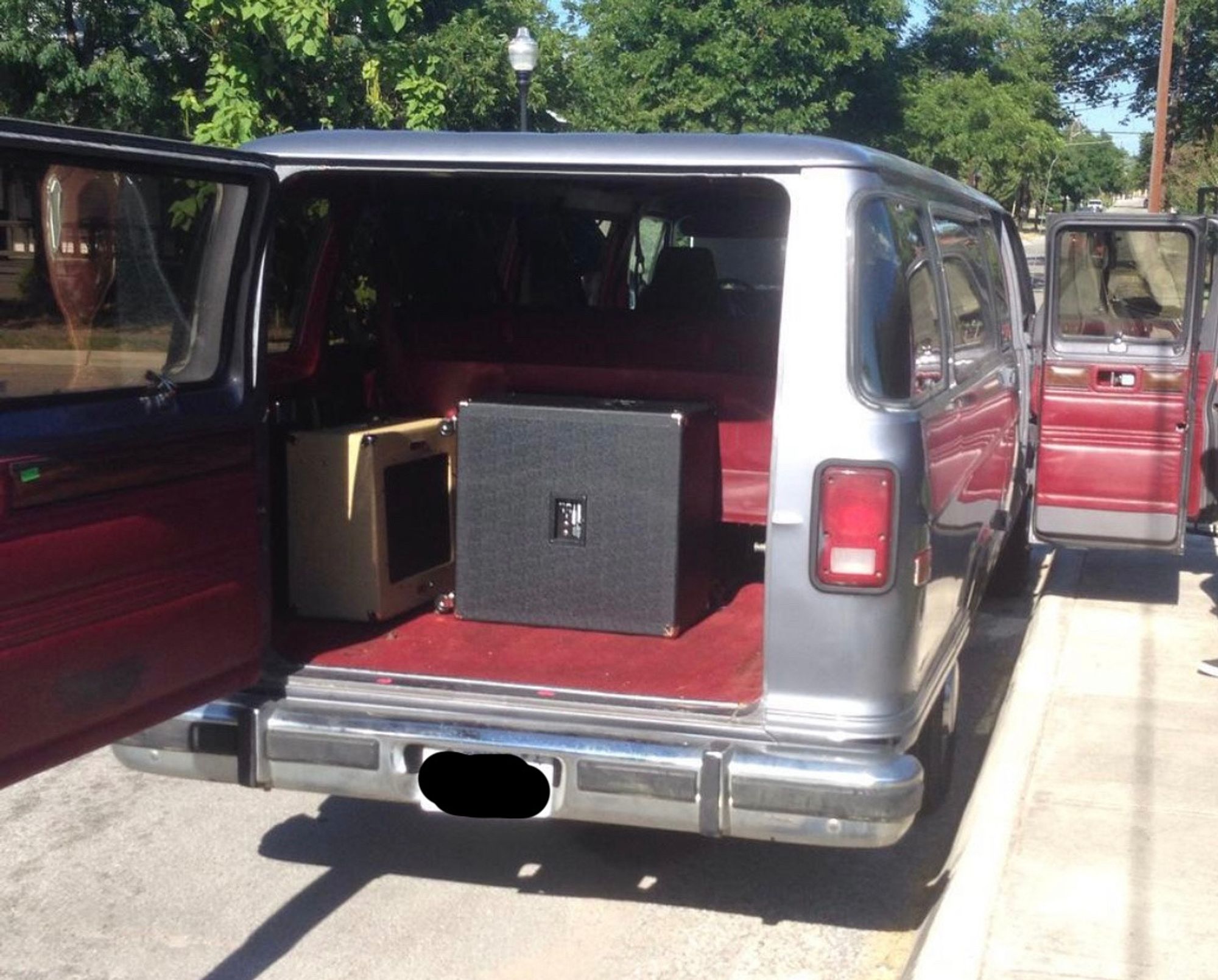 A photo of a dark gray ‘90s 15-passenger Dodge van with several doors open, revealing the dark red cloth interior.