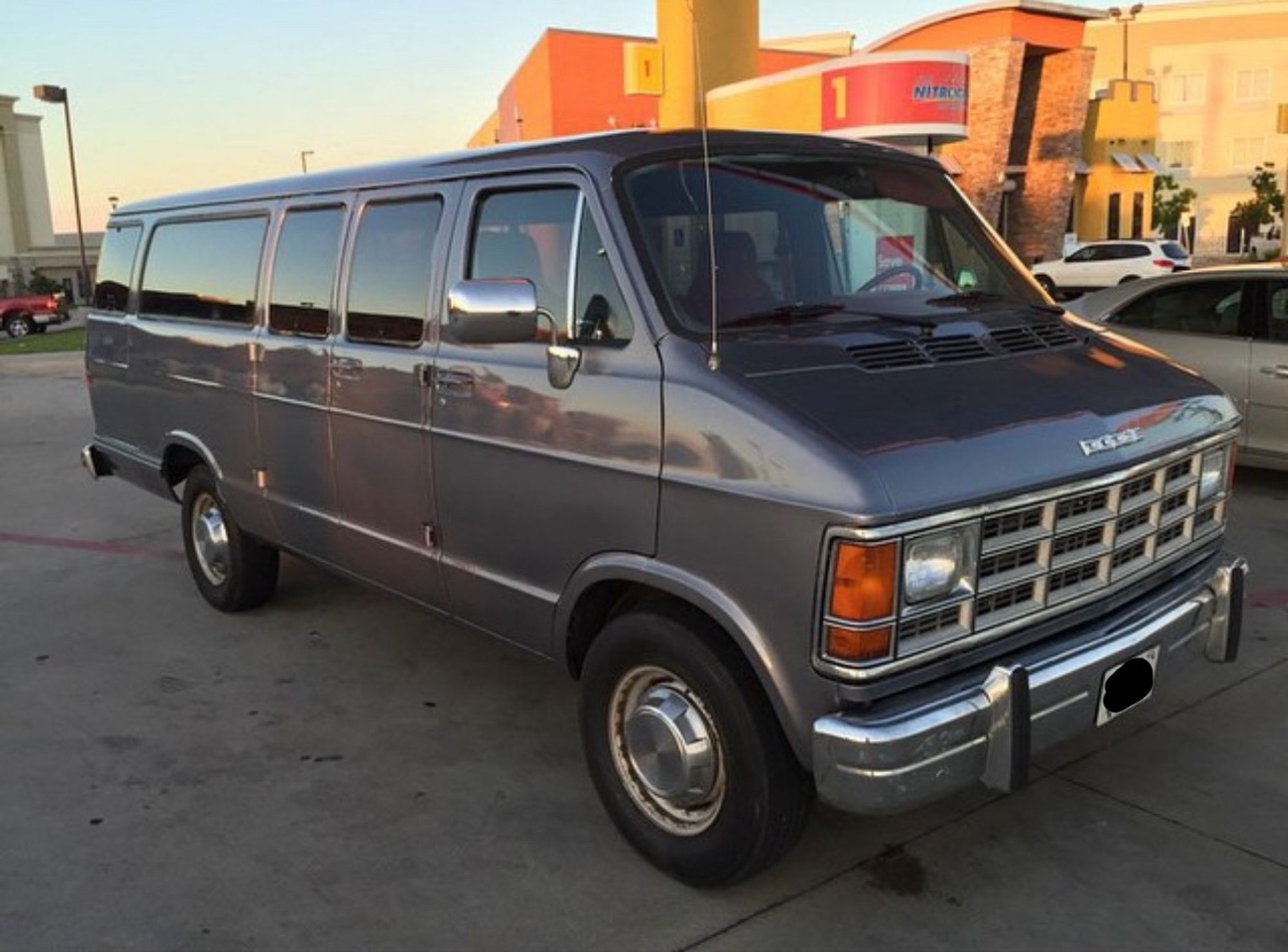 A photo of a dark gray ‘90s Dodge 15-passenger van parked in a parking lot.