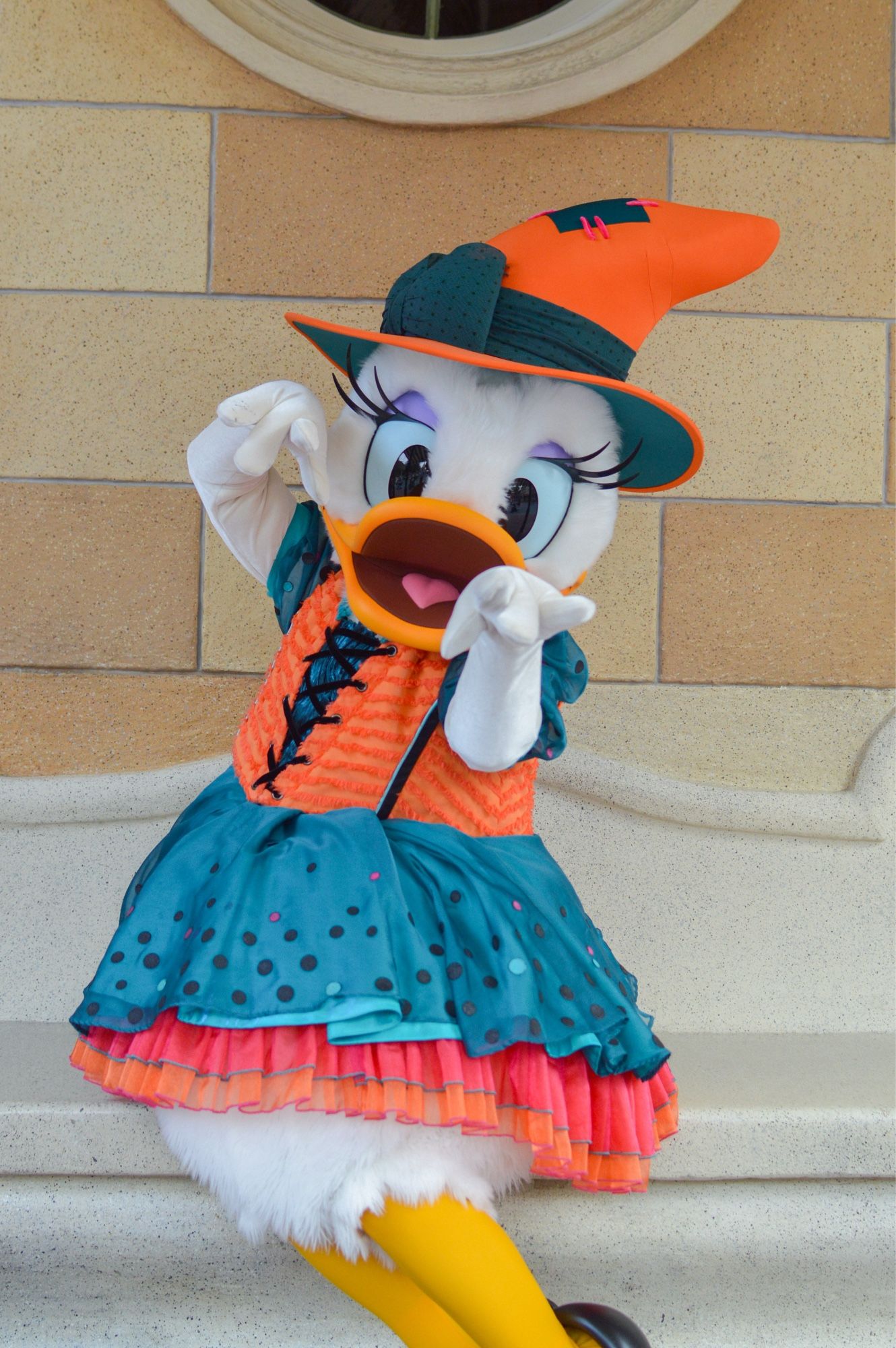 Daisy Duck dans un déguisement de sorcière orange et bleu, elle jette un sort à la caméra