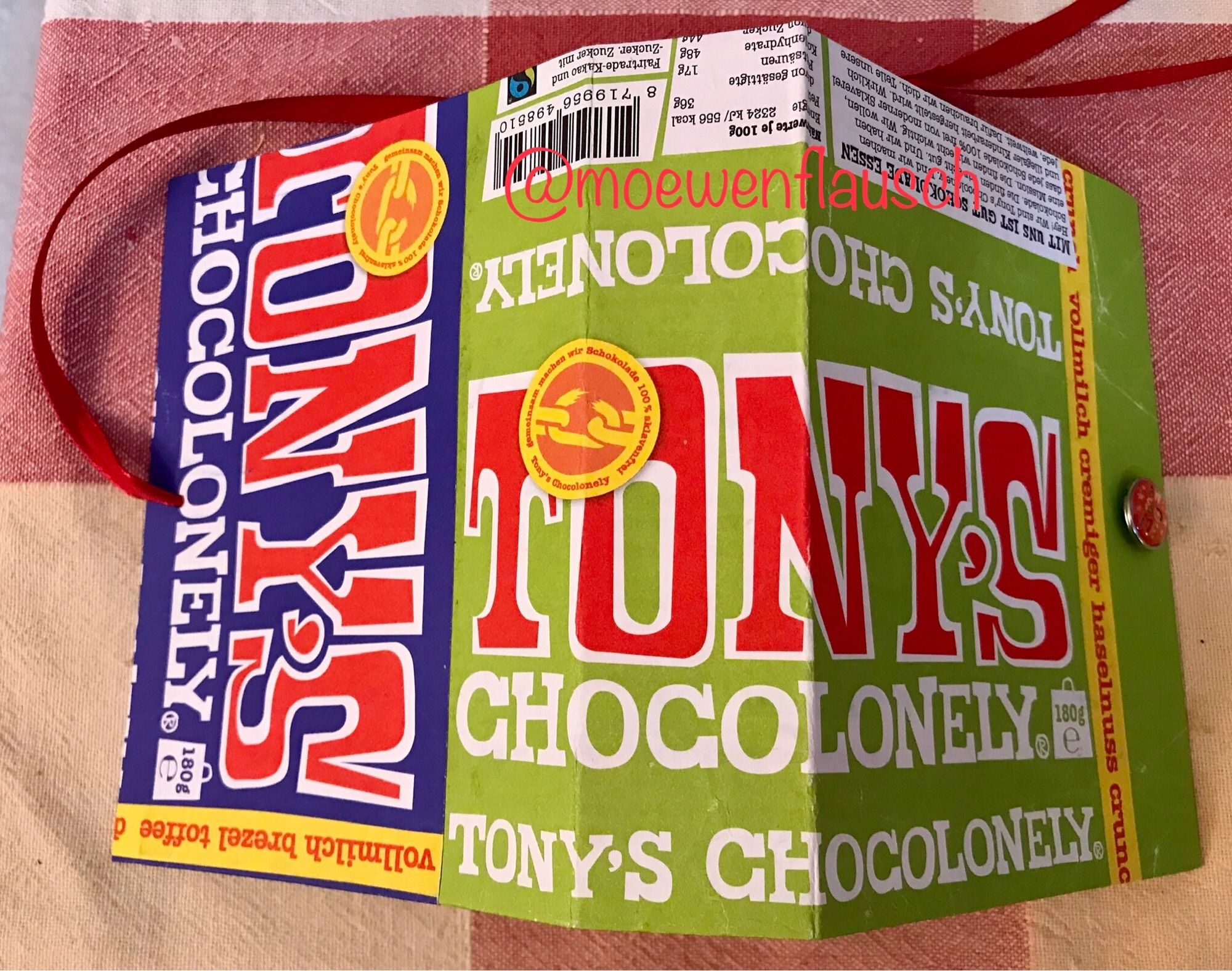 Umschlag des Notizbuches von außen: gestaltet mit Einwickelpapier von grüner und blauer Tony‘s Chocolonely. Rechts mittig am Rand ist ein rotbunter Brad zu erkennen, links schaut ein rotes Band aus dem Buch heraus.