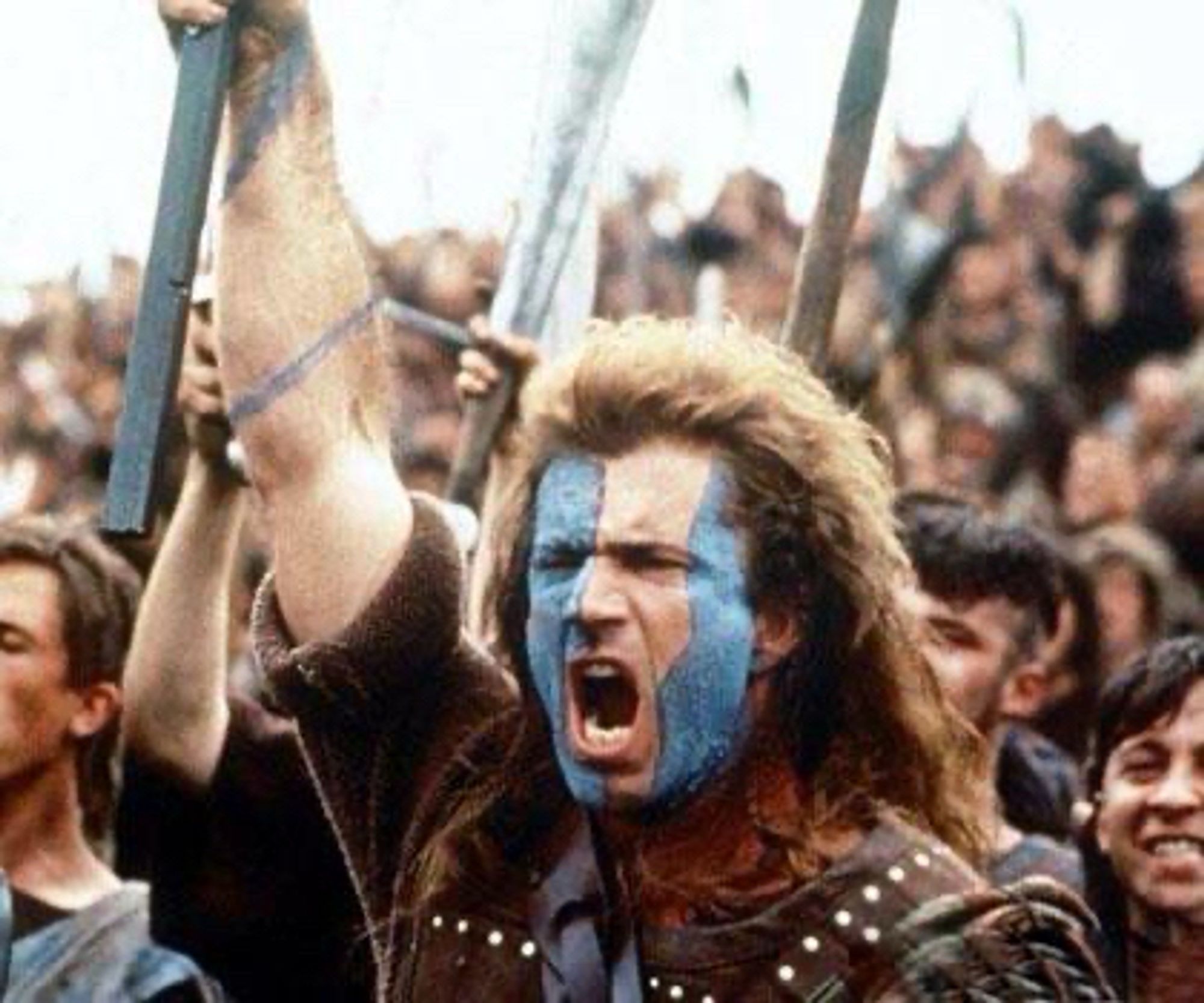 Mel Gibson in Braveheart. Er hat das Gesicht in blau und weiß geschminkt und den Arm nach oben gereckt.