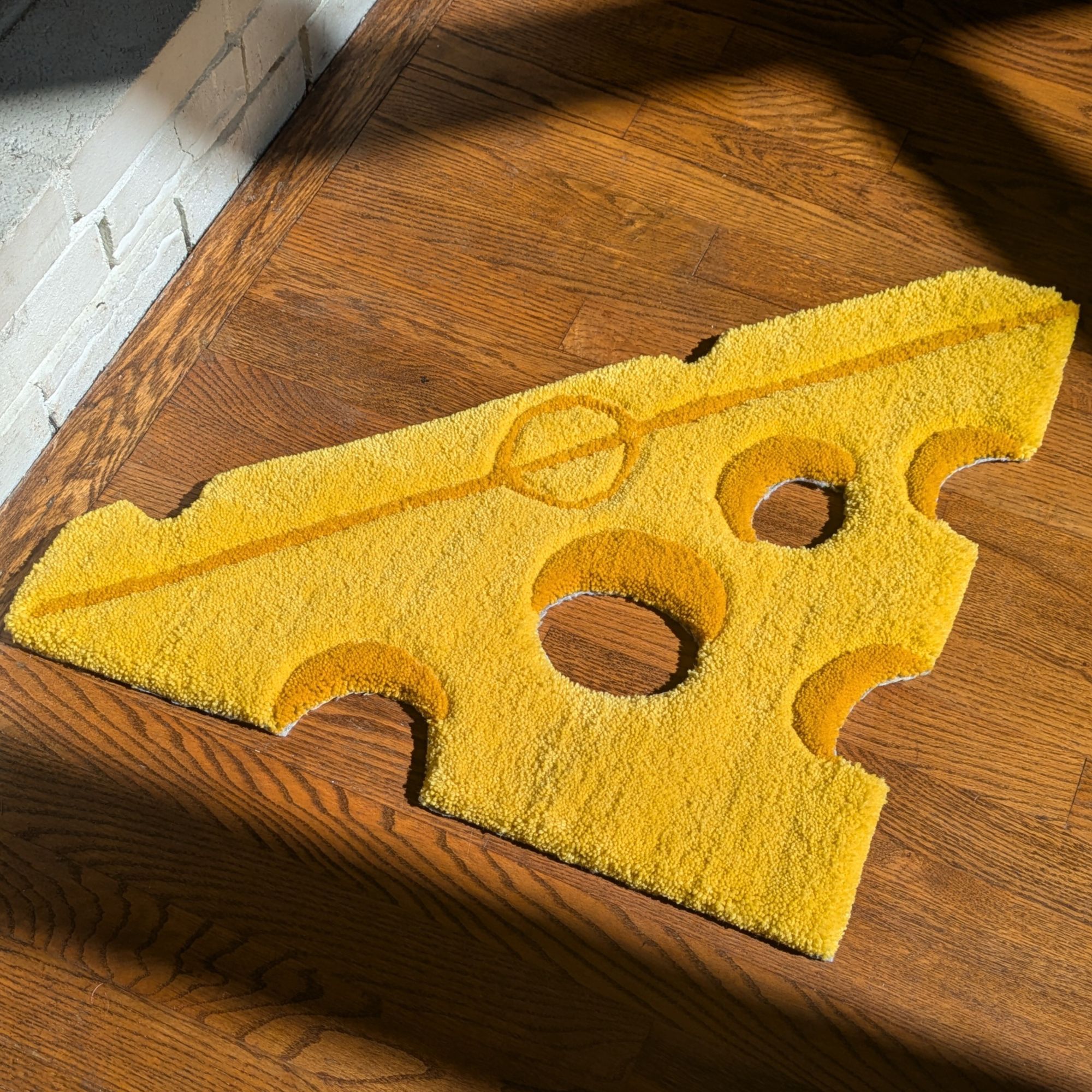 A rug in the shape of a block of cheese lays on a wood floor