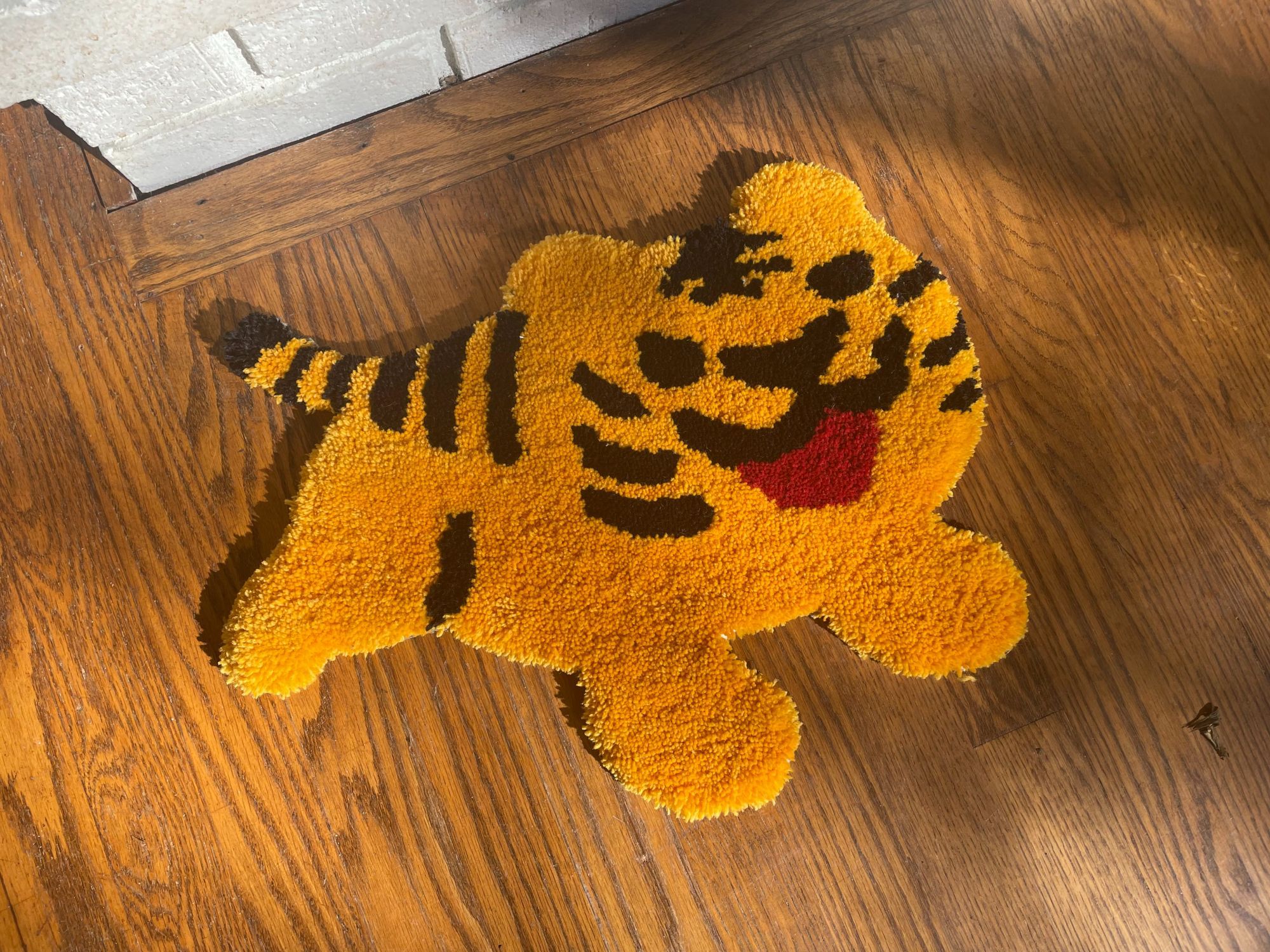 A rug of the Android emoji for tiger - yellow, striped, and with an open mouth - sits on a wood floor