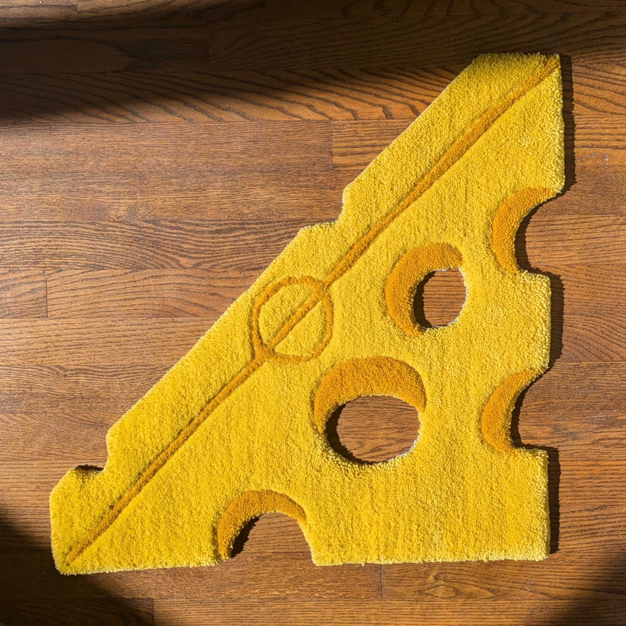 A rug in the shape of a block of cheese lays on a wood floor