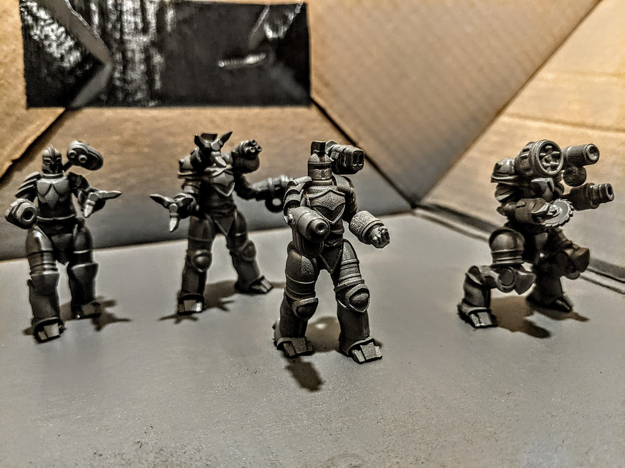 Four Titans in a cardboard box coated with a grey primer. These Titans were sculpted by Jason Miller. 