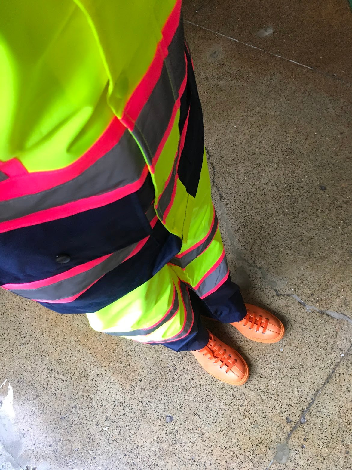 photo taken at an angle of.a cropped high viz yellow pink and black jacket and pants, orange boots.