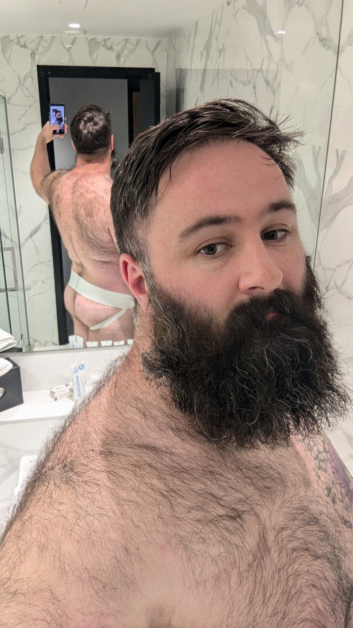 Arthur standing in front of a hotel mirror with his jockstrapped butt shown in the reflection