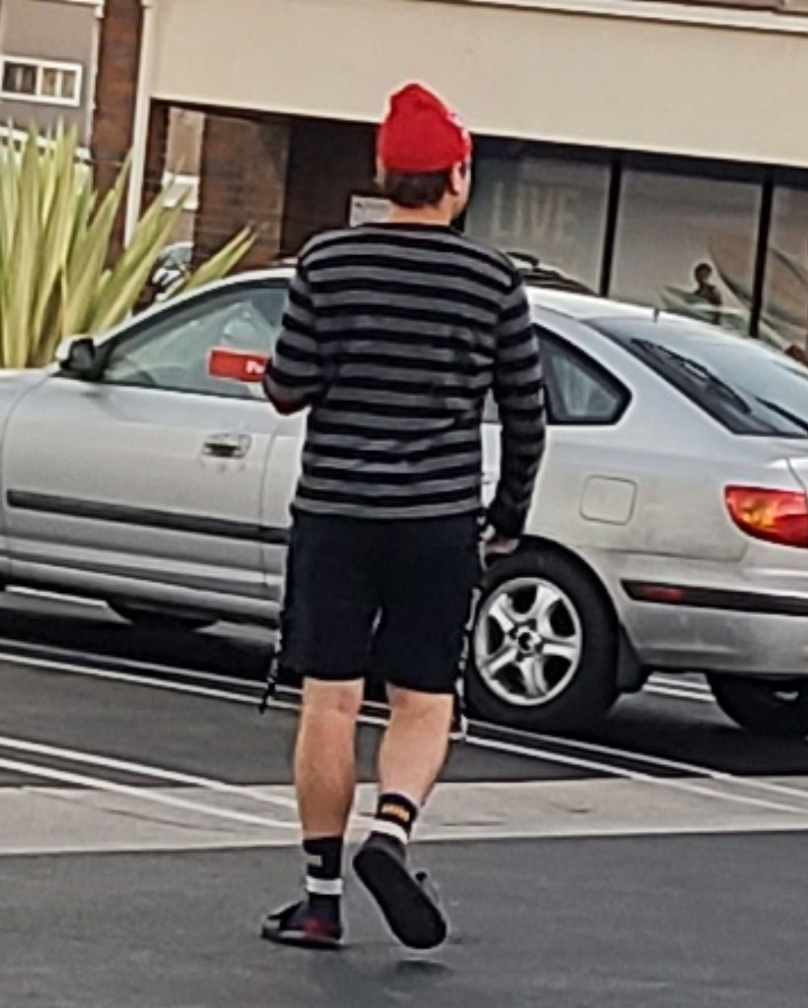 a white person, seen from behind, wearing a red knit stocking cap, a black & grey horizontal striped shirt  amd black shorts.