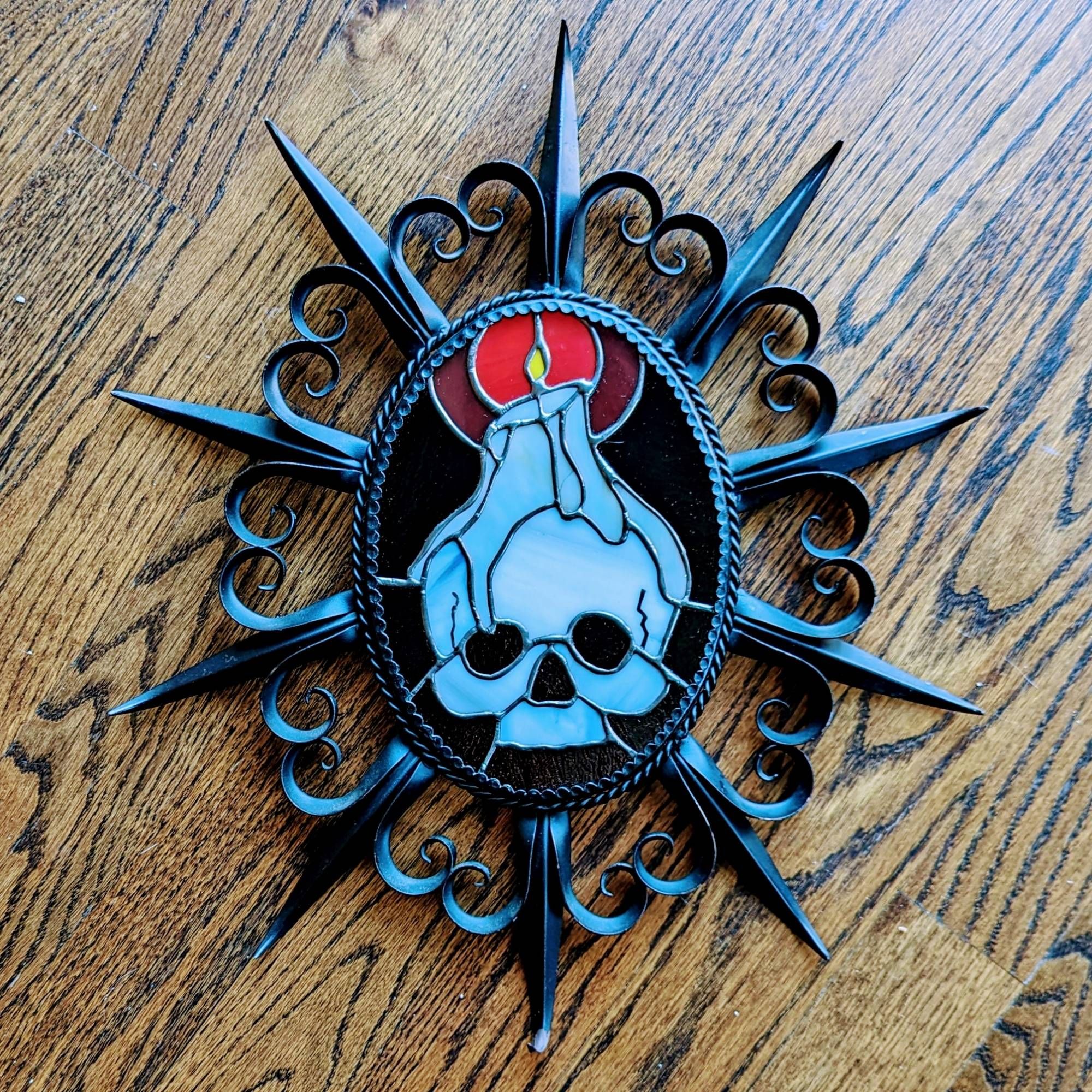 Stained glass of a skull with a lit candle perched on top in a spiked wrought iron frame