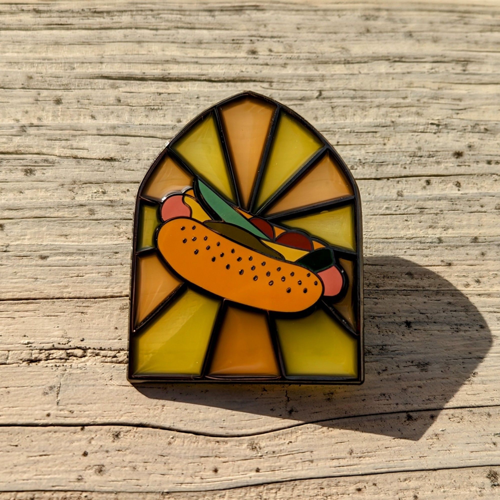 An enamel pin of a Chicago style hotdog in a cathedral window