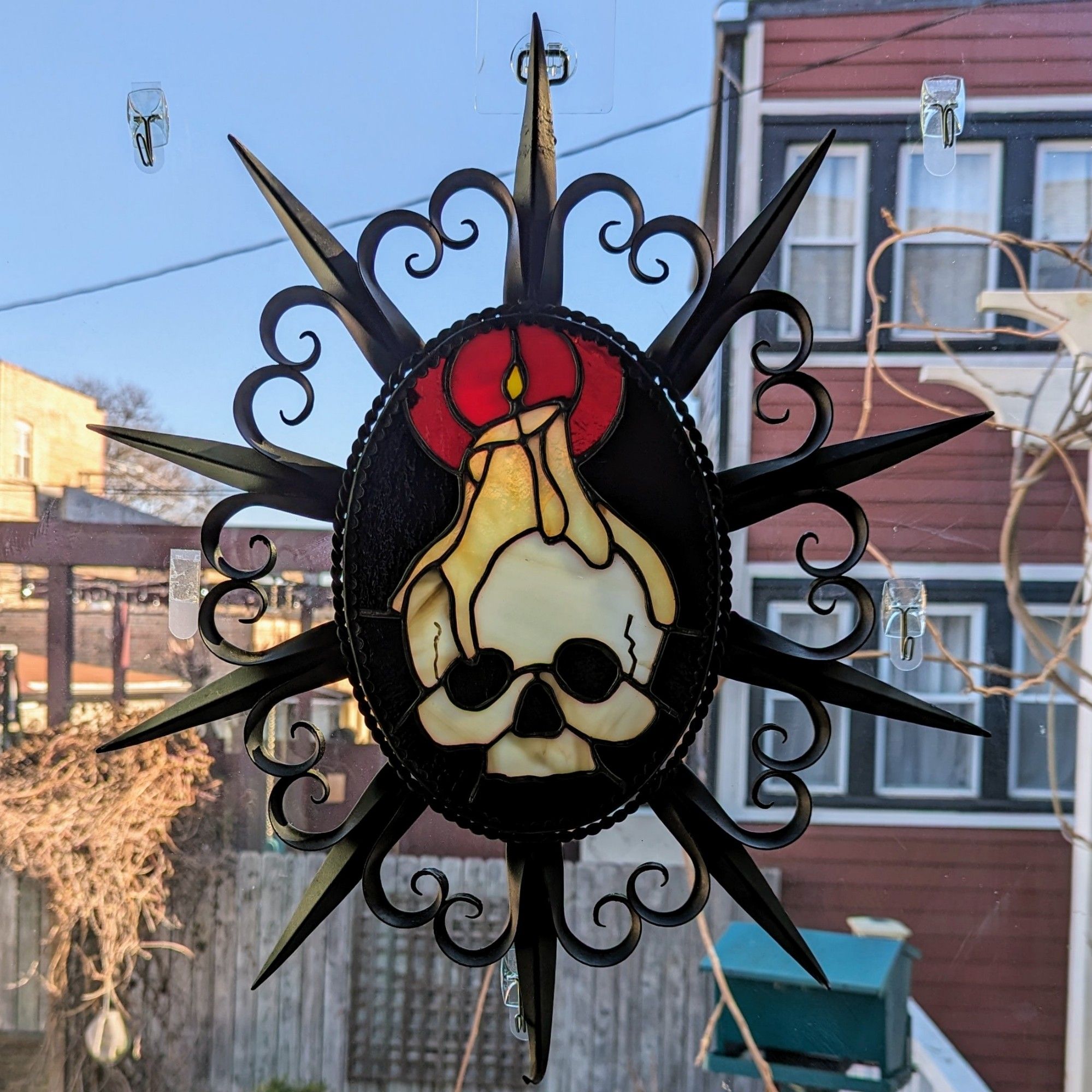 Stained glass of a skull with a lit candle perched on top in a spiked wrought iron frame