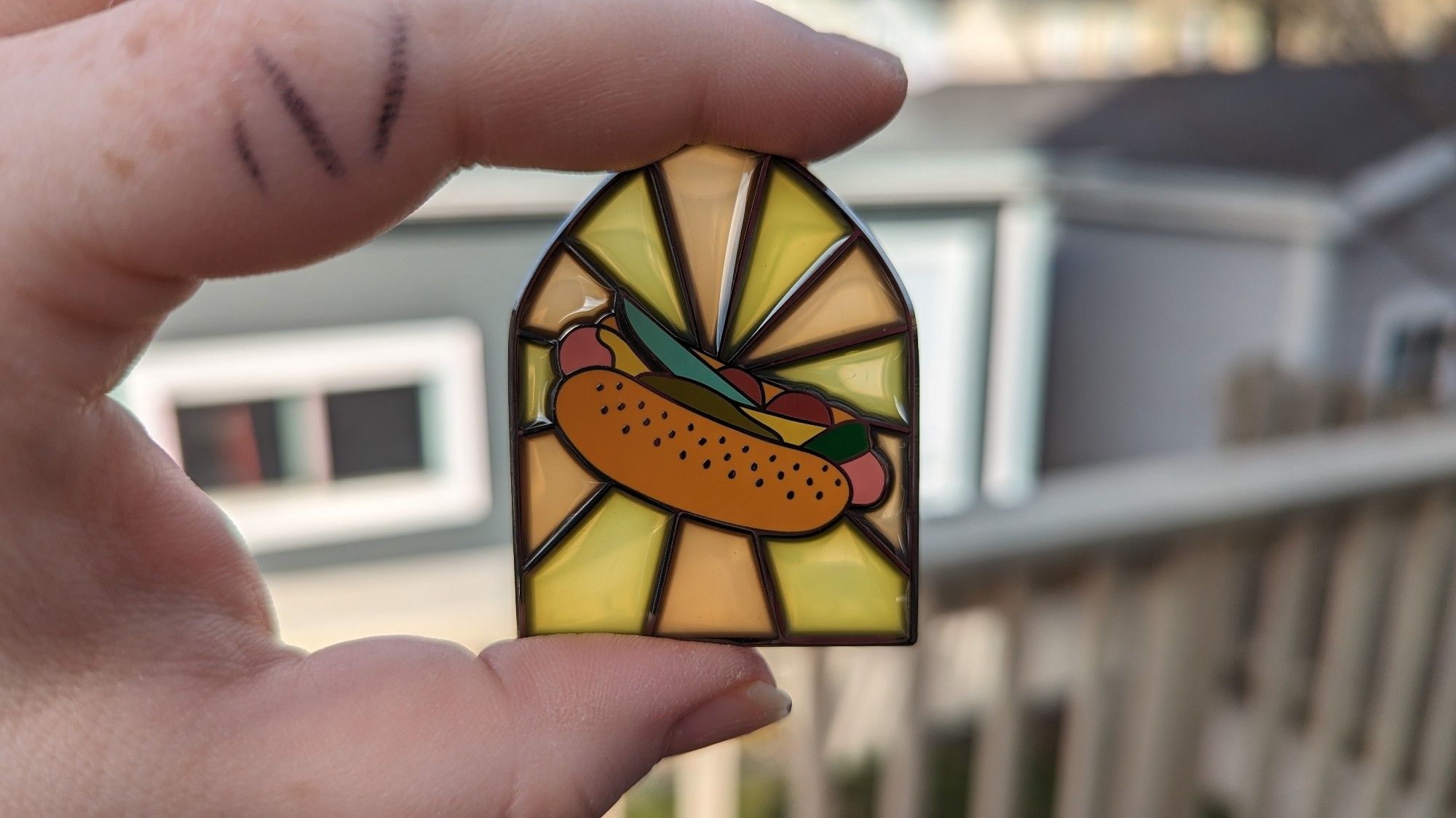 A backlit enamel pin of a Chicago style hotdog in a cathedral window showing that it is translucent