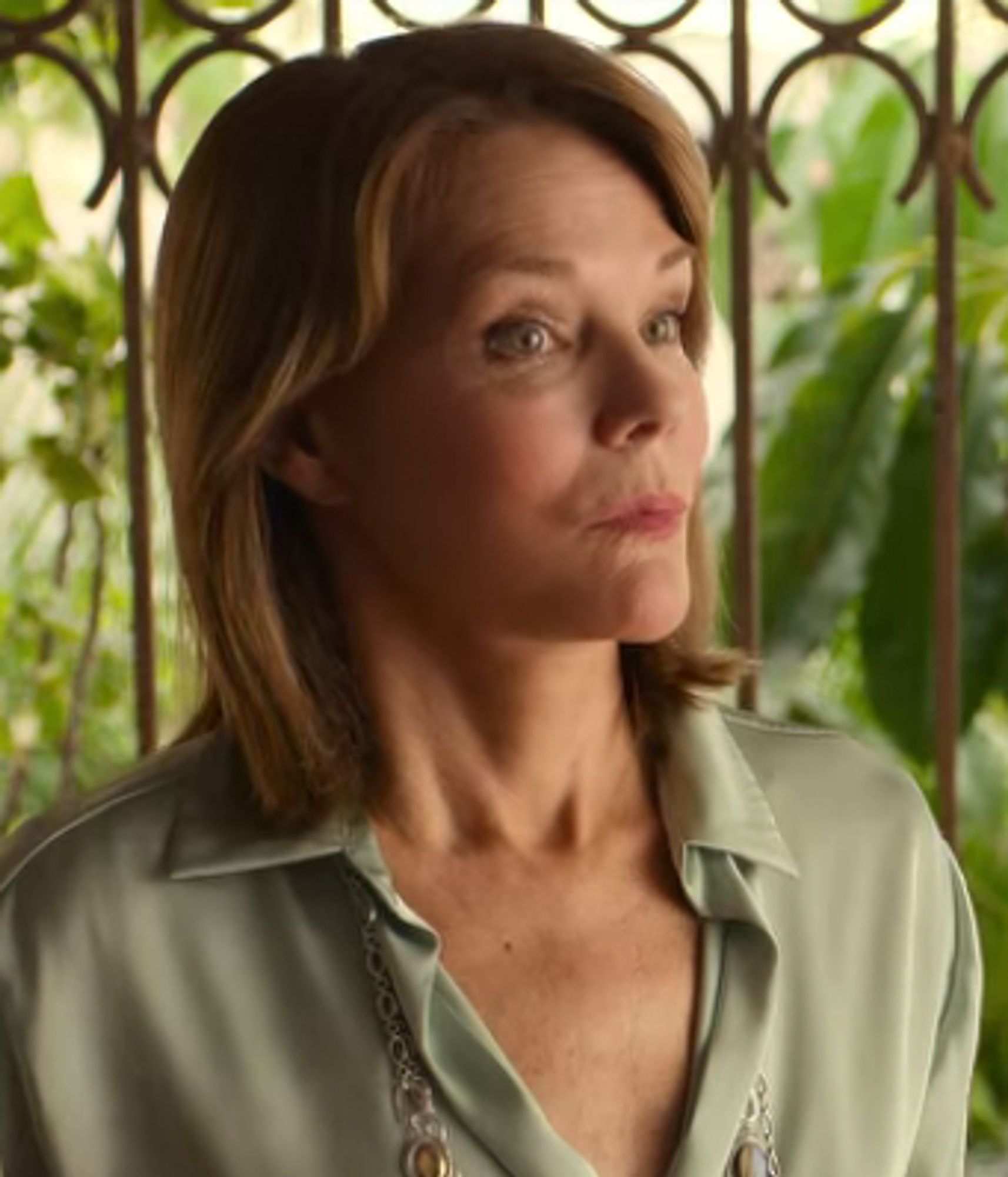 Woman in shoulder-length hair in a grey-green? button blouse with the collar open. Listening intently to Diana Nyad as she talks incessantly about herself at her birthday party.