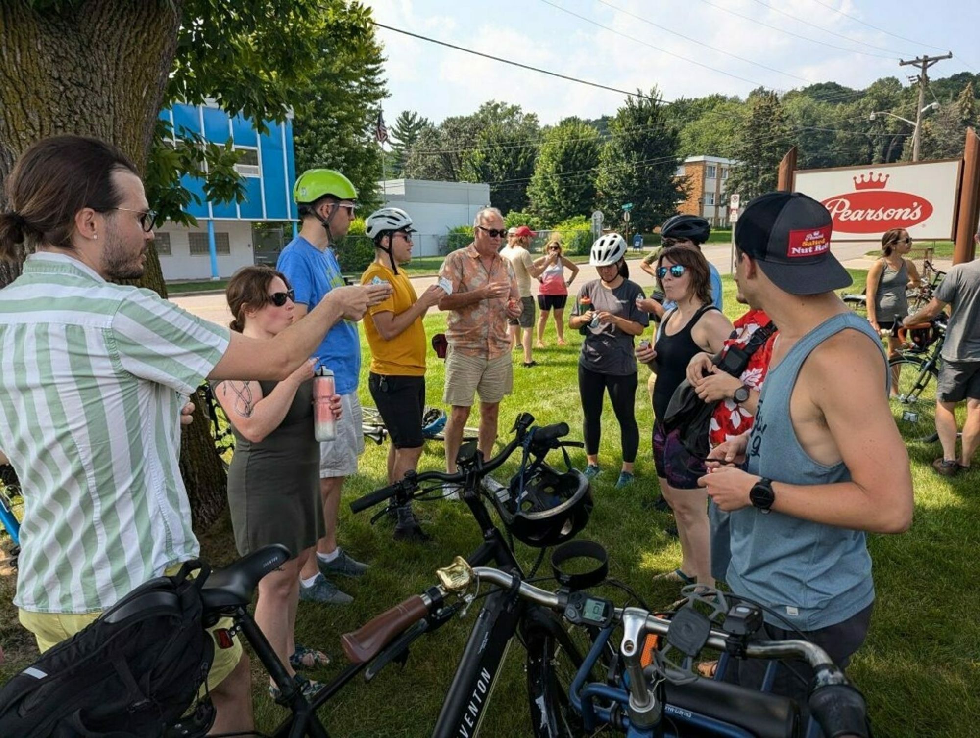 Bicyclists in a circle eating Salted Nut Rolls, in front of a sign for Pearson's Candy Company