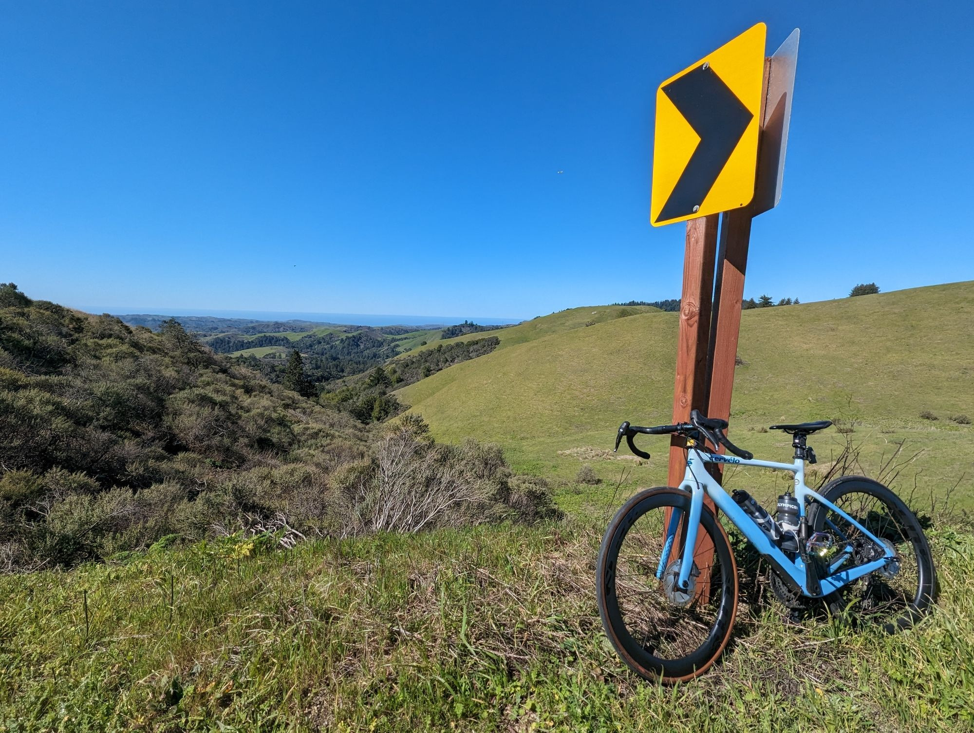 My bike leaning against a signpost looking over verdant Bay Area hills.